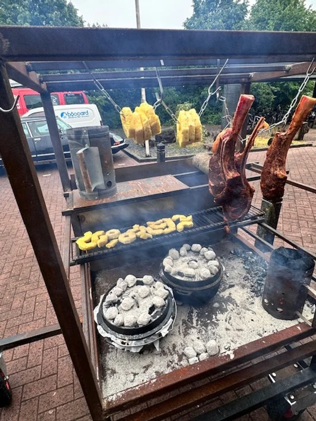 Outdoor barbecue grill with meat, vegetables, and bread being cooked.