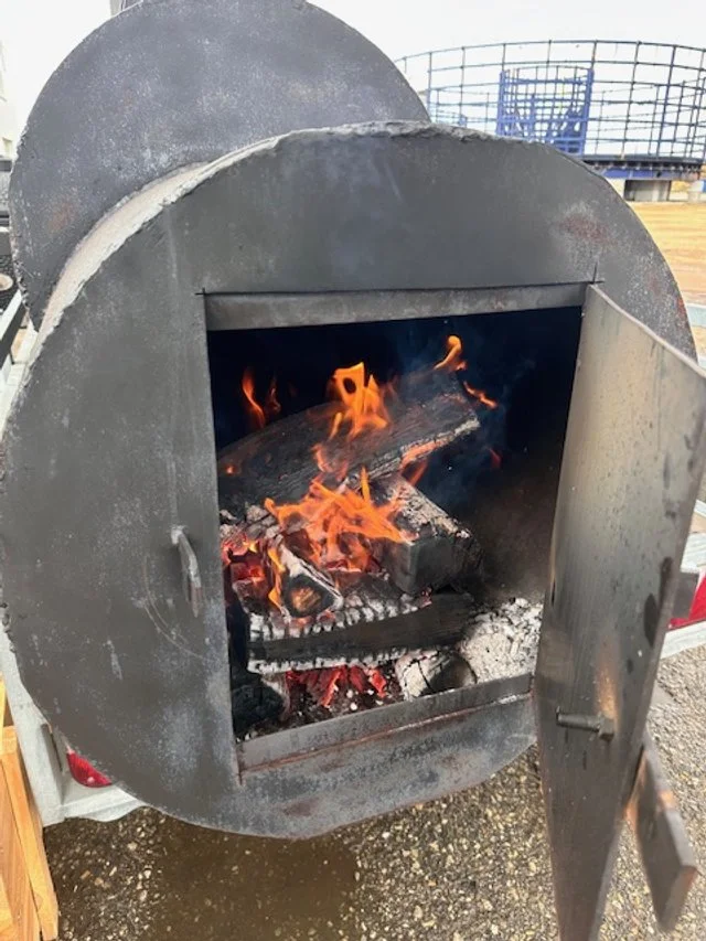 A portable metal fire pit with a fire burning inside, placed outdoors on a concrete surface.