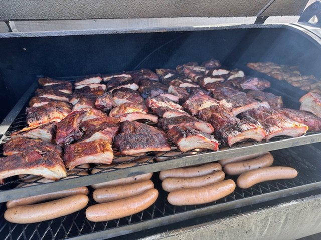 Pork ribs and sausages cooking on a barbecue grill.