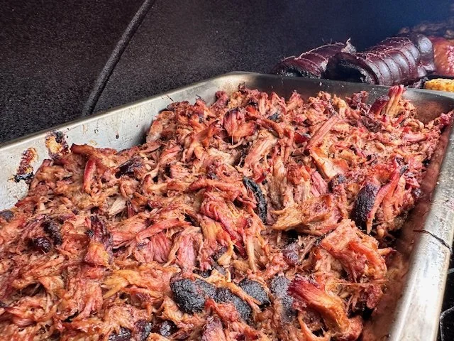 Shredded cooked barbecue pork in a metal tray with some darker burnt pieces, against a black background.