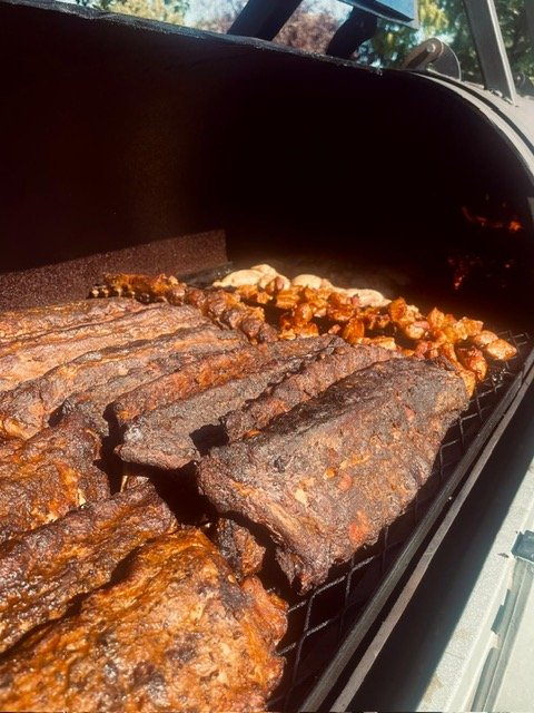 Beef ribs and chicken pieces cooking on a barbecue grill.