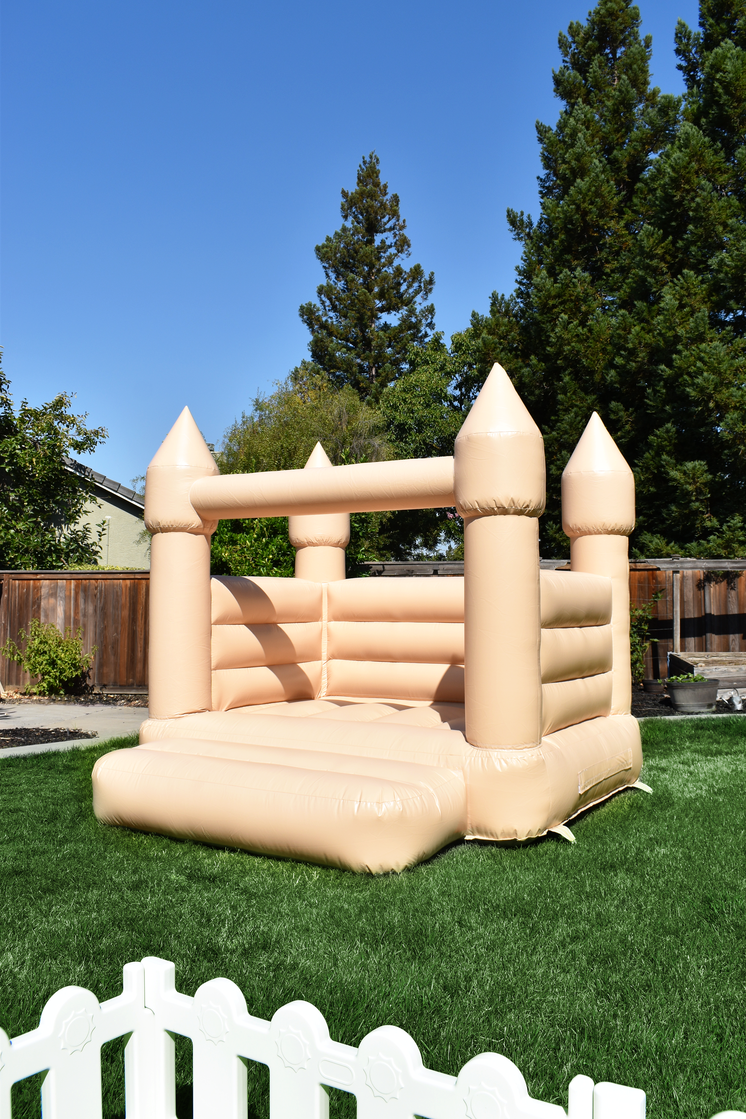 A beige inflatable bounce house resembling a castle in a backyard on a sunny day.