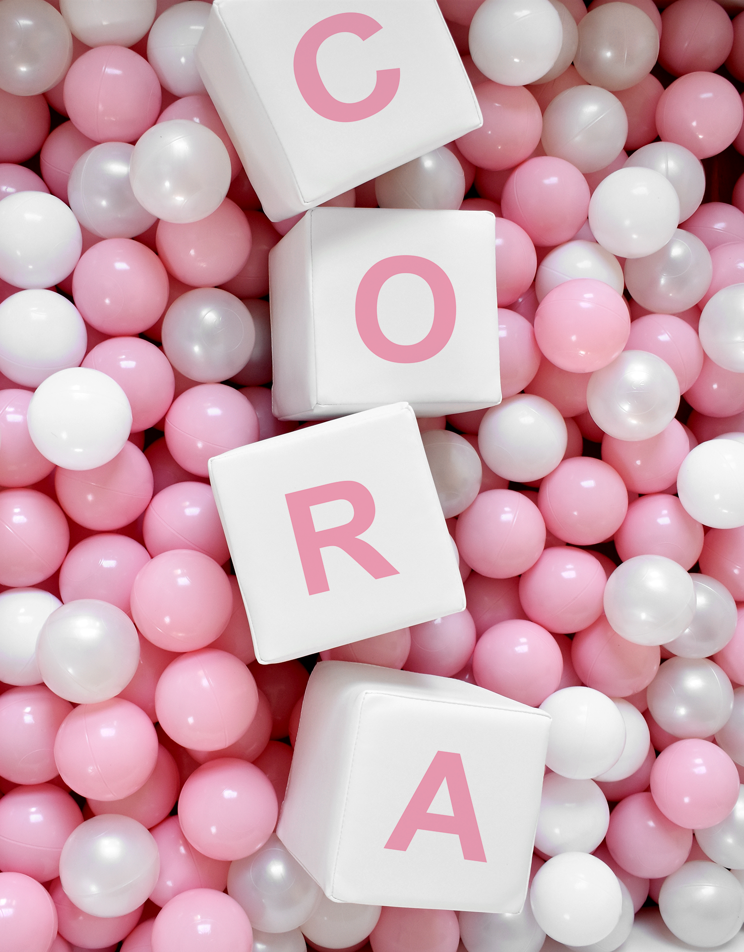 Pink, white, and pearl-colored plastic balls with four white blocks spelling out 'Cora' in pink letters.