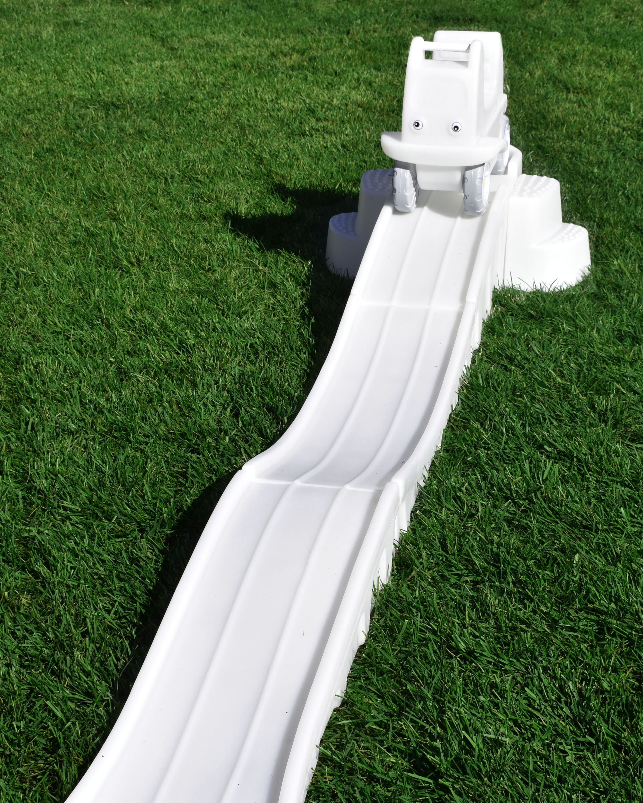 White plastic slide on green grass with a small grassy hill at top.