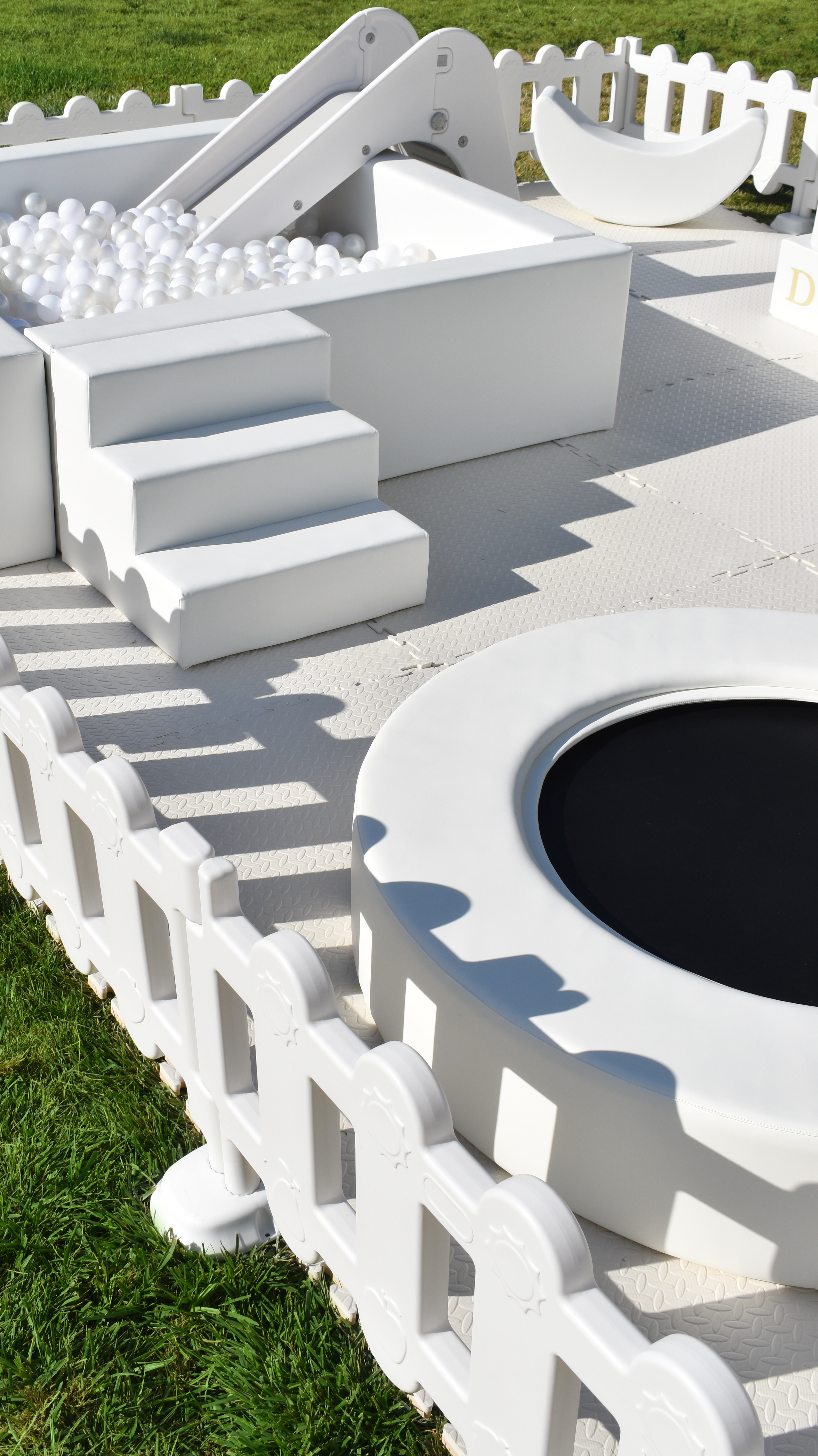 White children's soft play area with stairs, ball pit, trampoline, and garden fence on grass.
