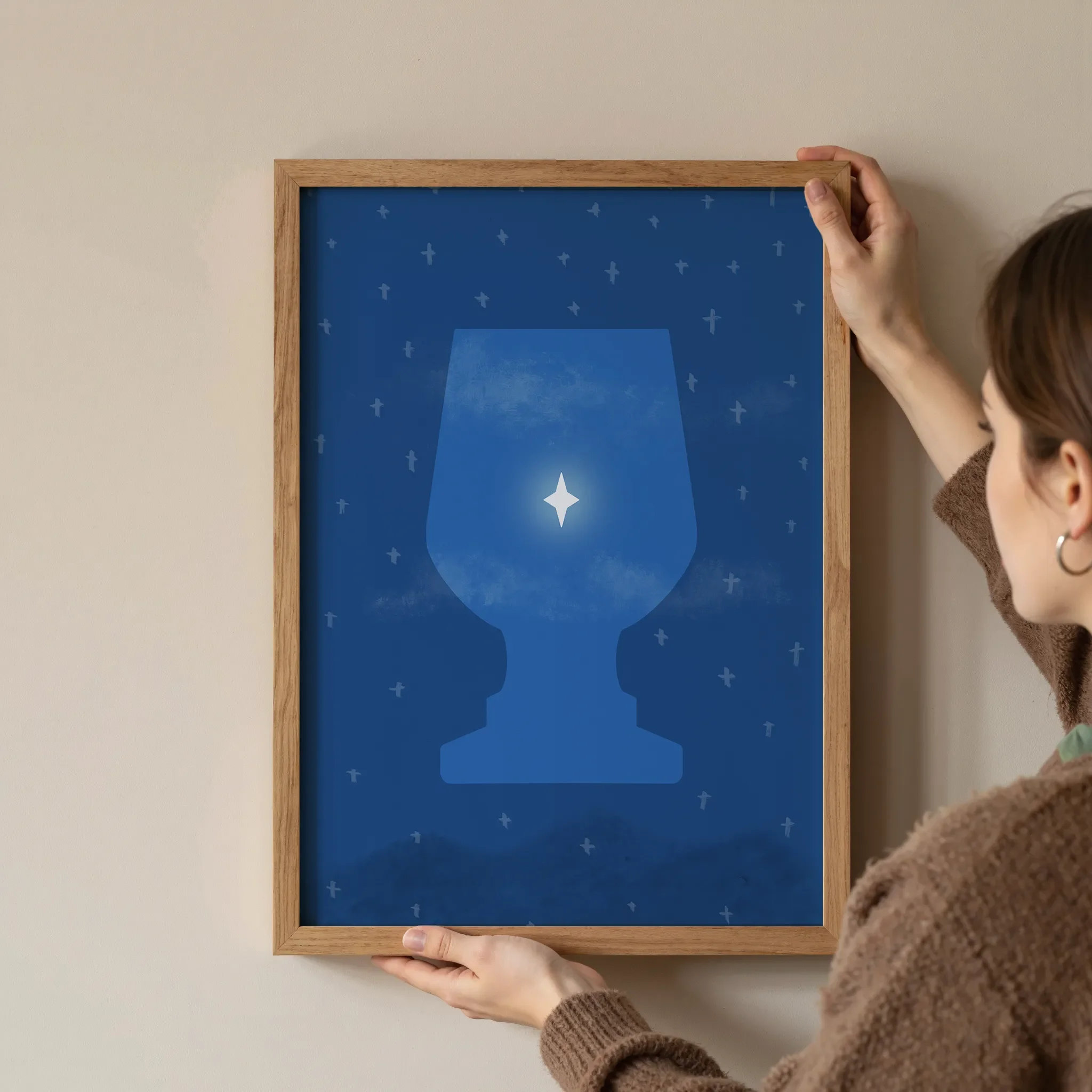 A surreal Star of Bethlehem print in a simple wooden frame is held at the corners by a young woman against a neutral wall.