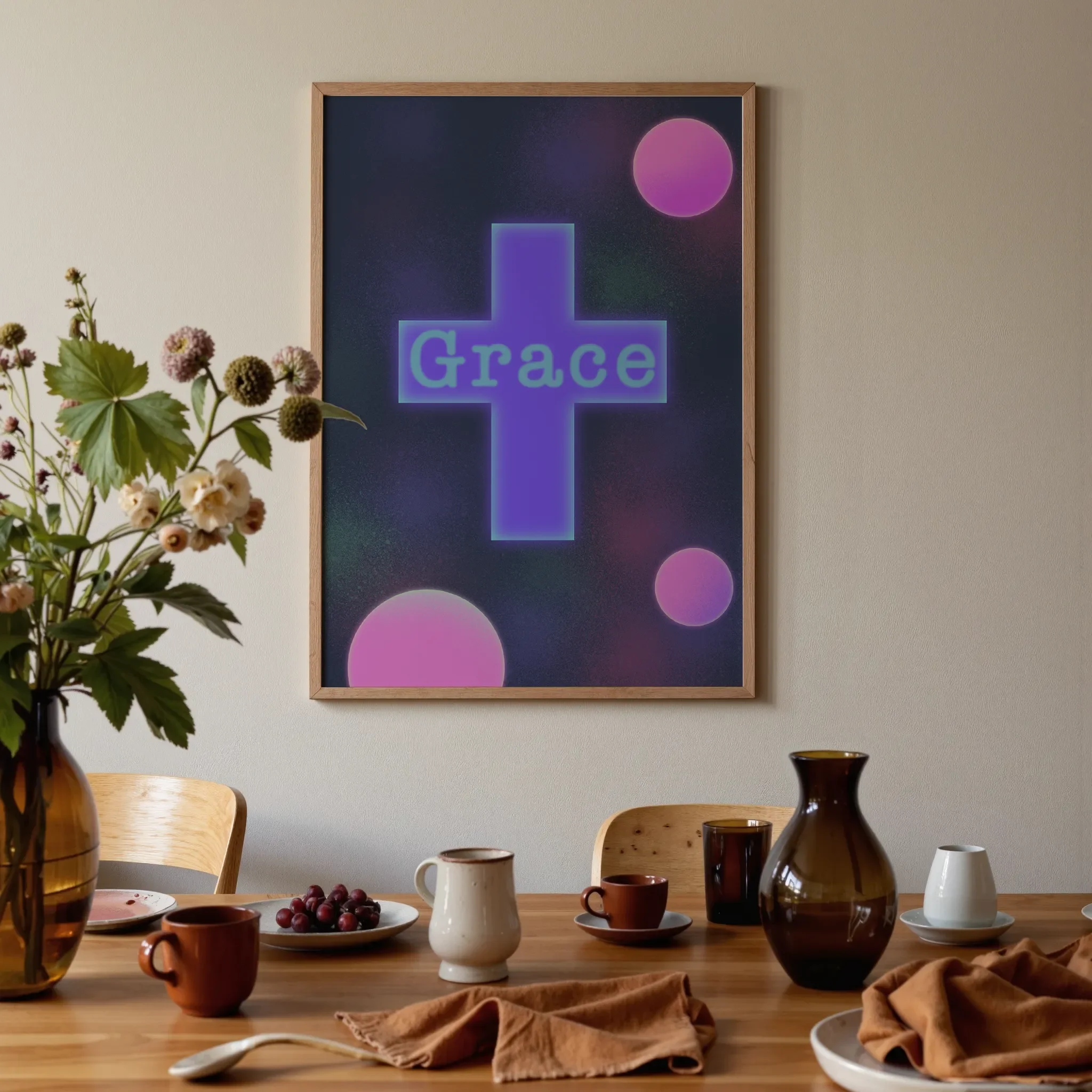 A colorful geometric cross print hangs above a warm wooden dining table in brown and orange tones. On the table are glass vases, ceramics, flowers, and fruits, softly lit by natural light.