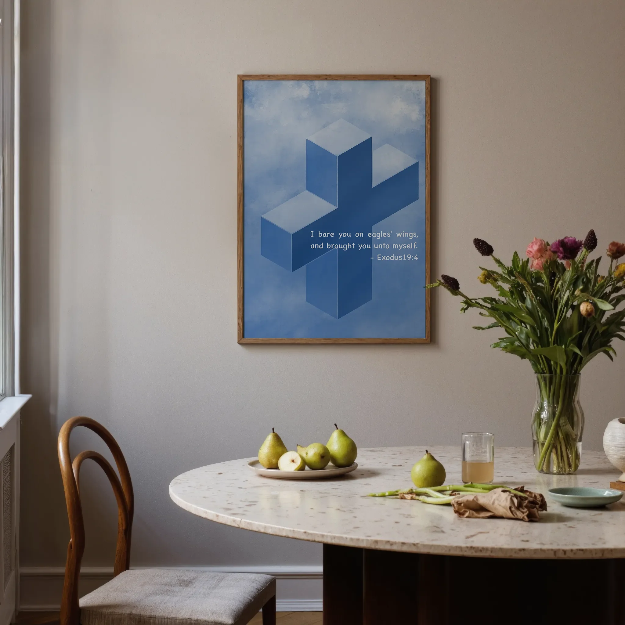 A Scripture wall art featuring a cross hangs on a neutral wall in a softly lit room. In front is a round stone table with glassware, ceramics, pears, and flowers. A chair sits on the left.