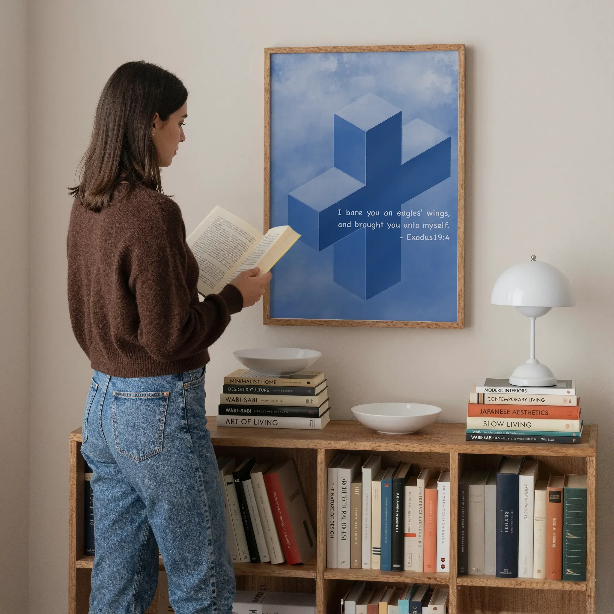 A Scripture wall art featuring a cross hangs above a wooden bookshelf in a softly lit room. A young woman stands nearby reading a book. On the bookshelf are books, a white lamp, and ceramic bowls.