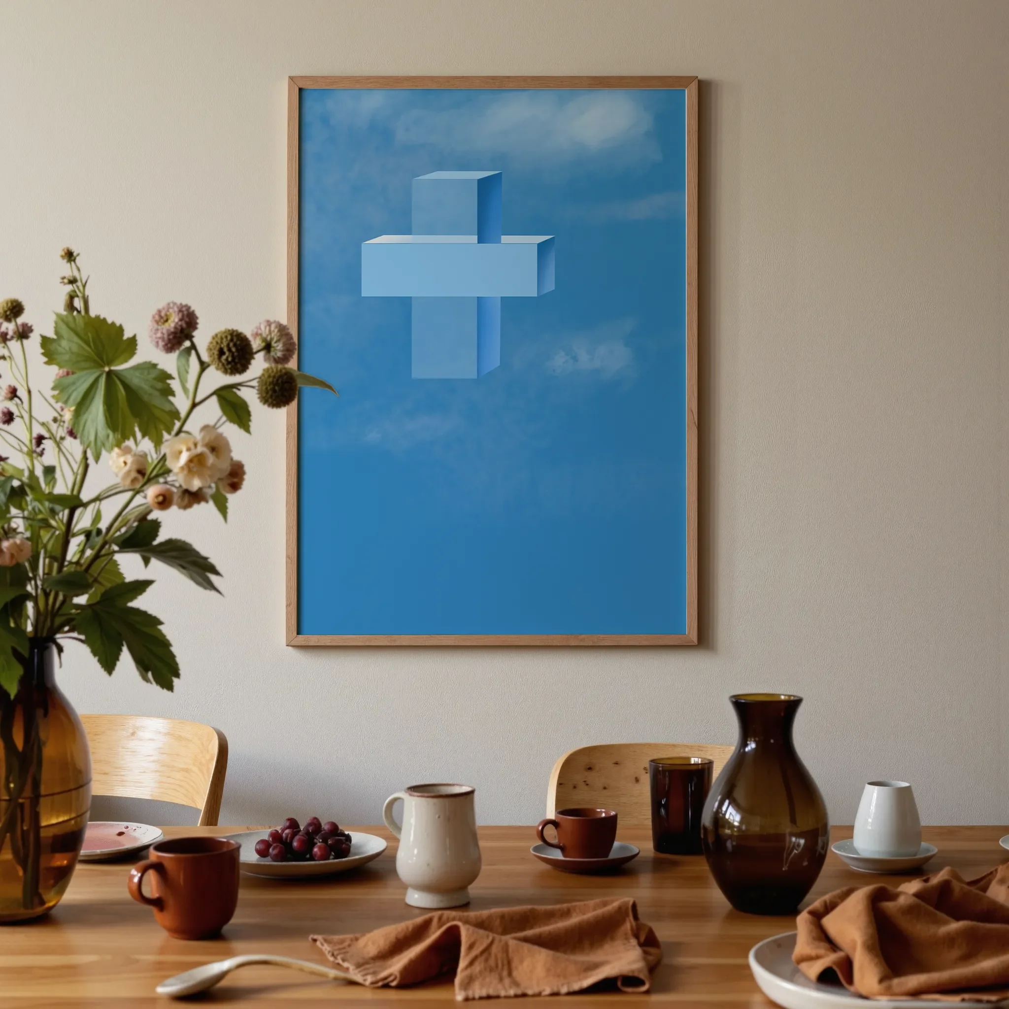 A cross print hangs above a warm wooden dining table in brown and orange tones. On the table are glass vases, ceramics, flowers, and fruits, softly lit by natural light.