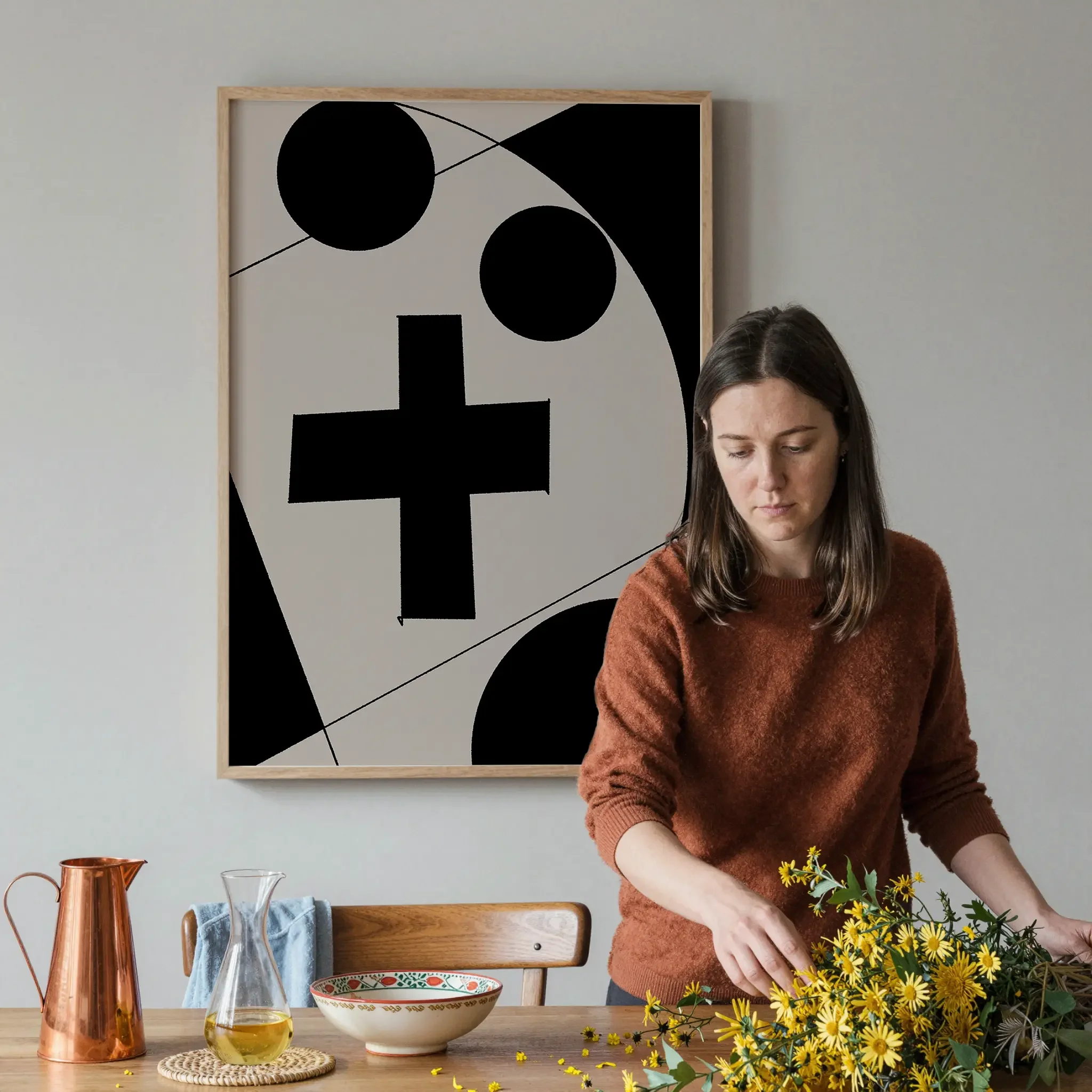 A Christian wall art print featuring cross art poster geometric minimalist design, shown in a dining space with a person arranging the table with flowers and tableware.
