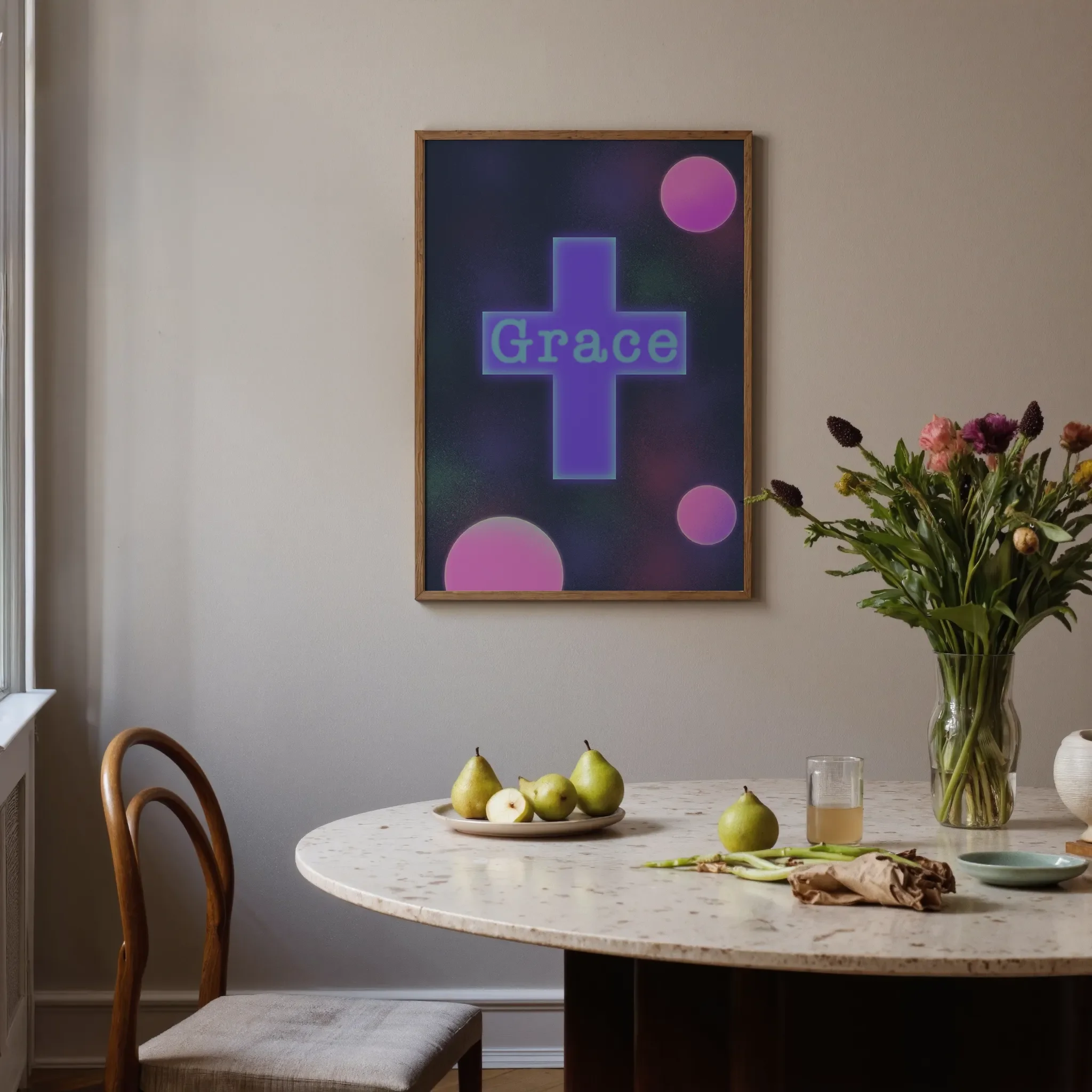 A colorful geometric cross print hangs on a neutral wall in a softly lit room. In front is a round stone table with glassware, ceramics, pears, and flowers. A chair sits on the left.