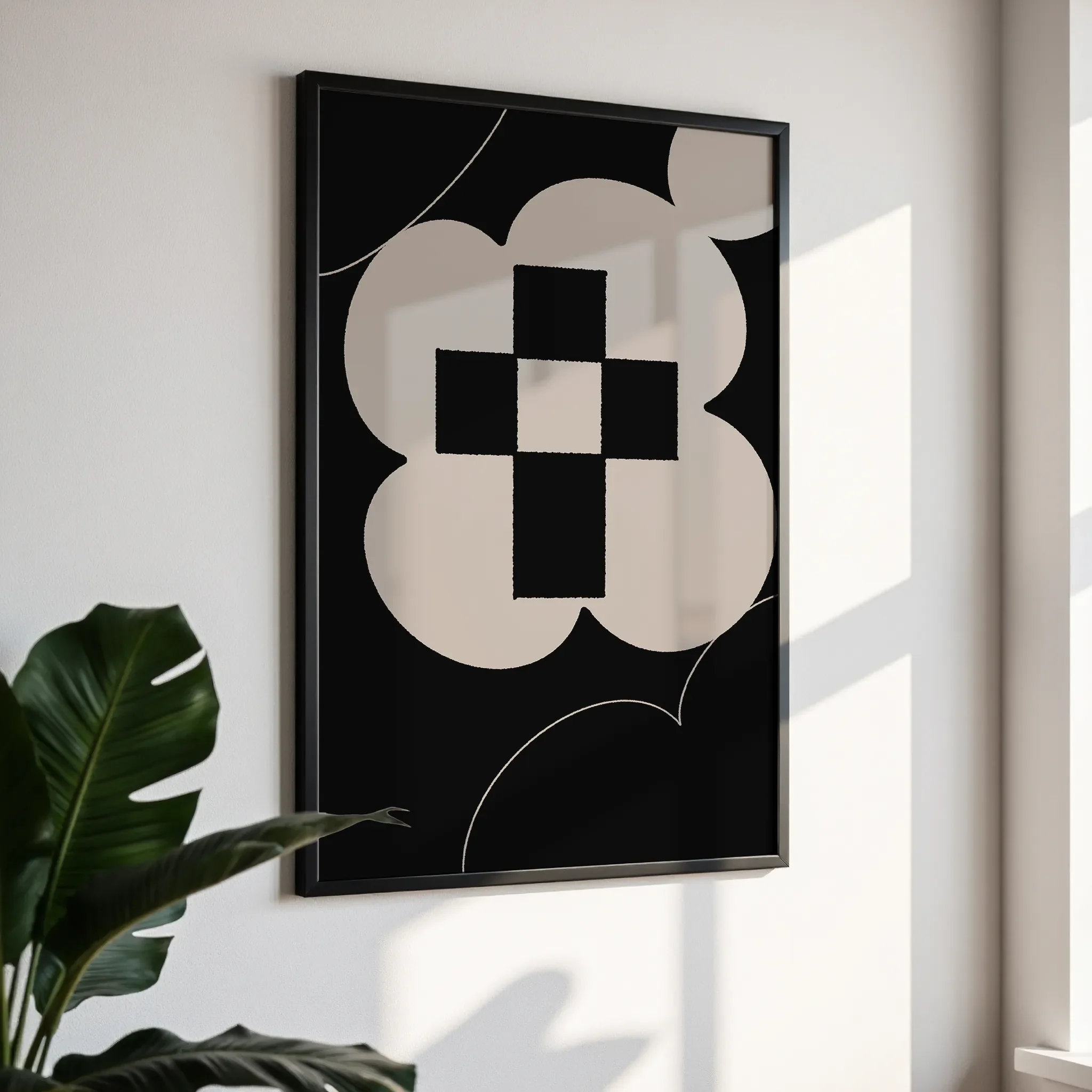 Framed wall art in a simple black frame, photographed from an angled view against a white wall with direct sunlight.