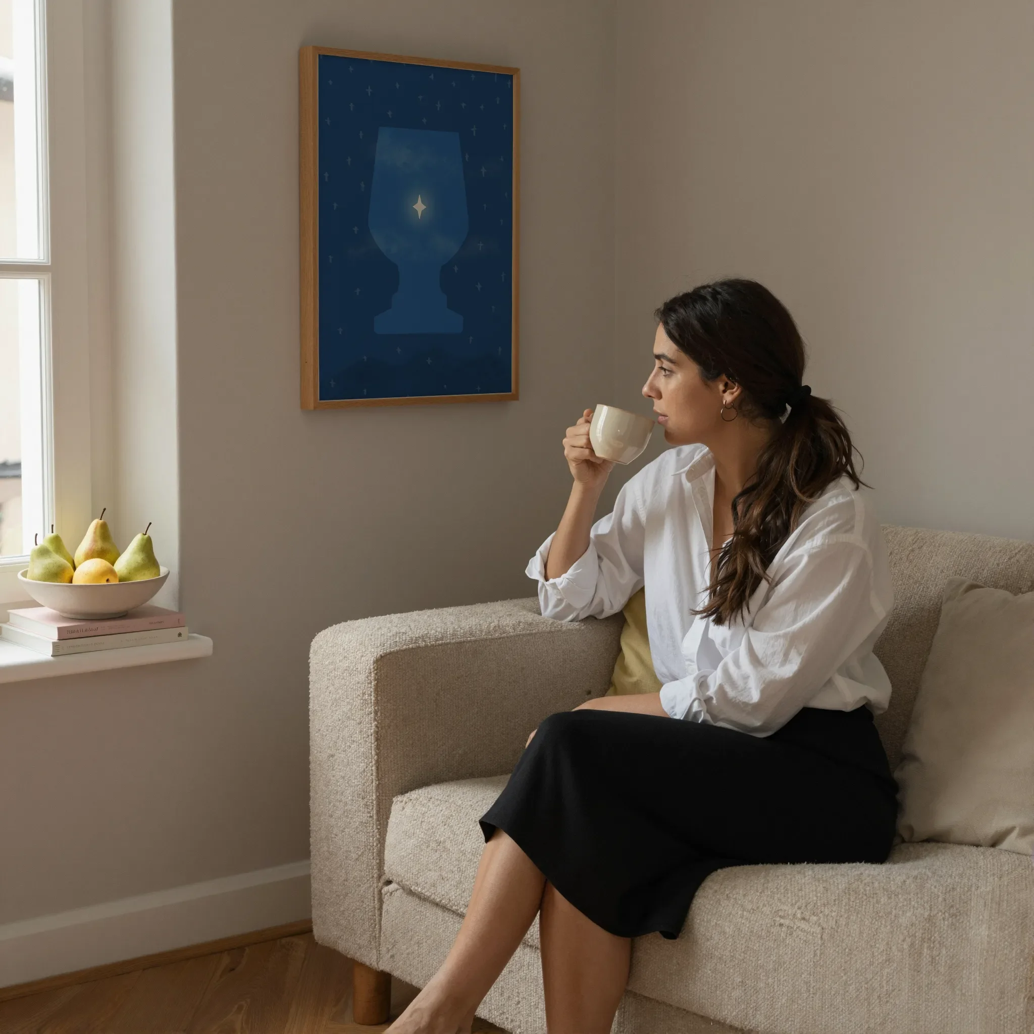 A surreal Star of Bethlehem print hangs on a neutral wall in a cozy living room. A woman sits on a sofa holding a ceramic cup and looking out the window. Pears and books rest on the windowsill.