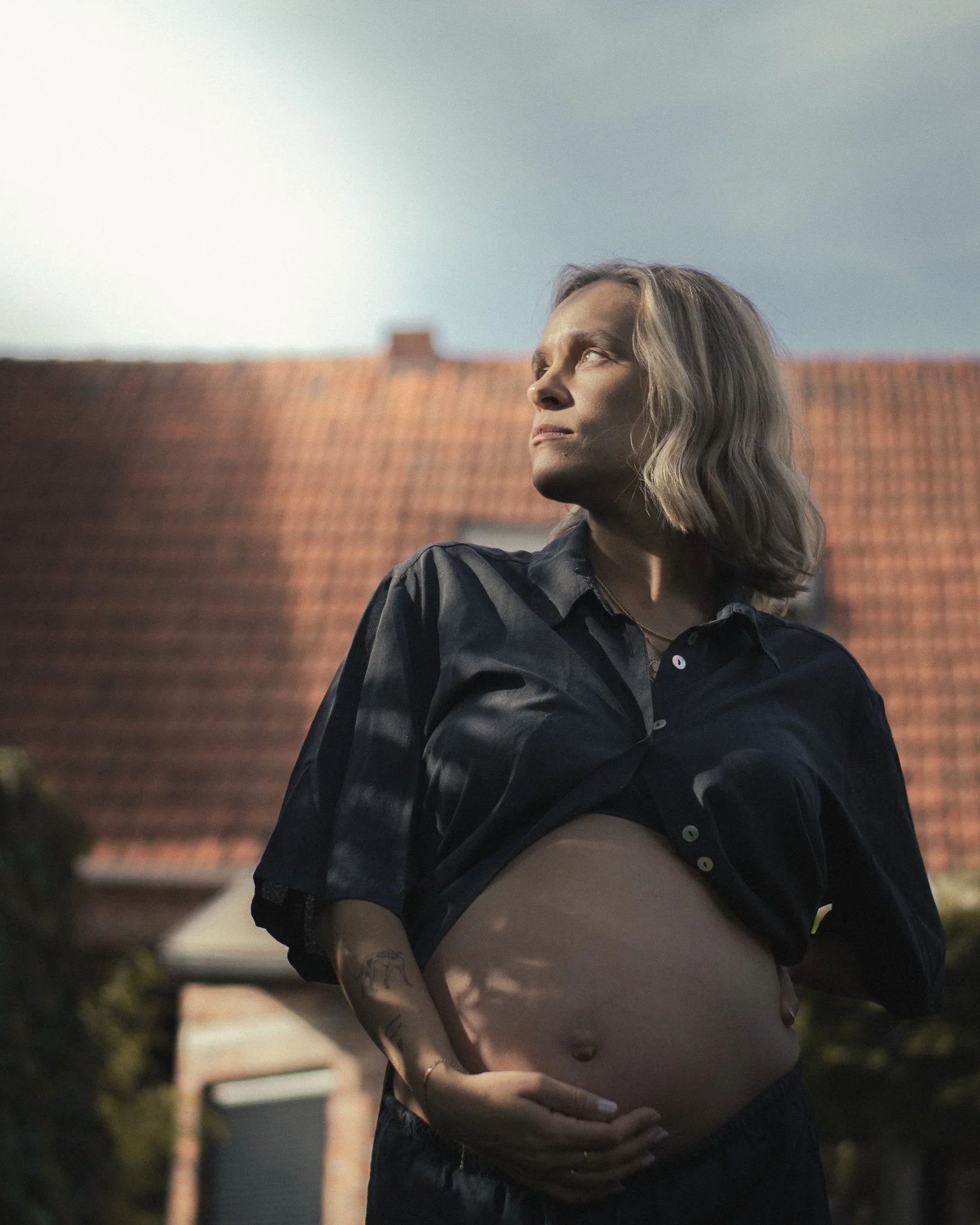 Vrouw zit ontspannen op een bank, haar hand rust op haar buik, terwijl ze naar het raam kijkt.