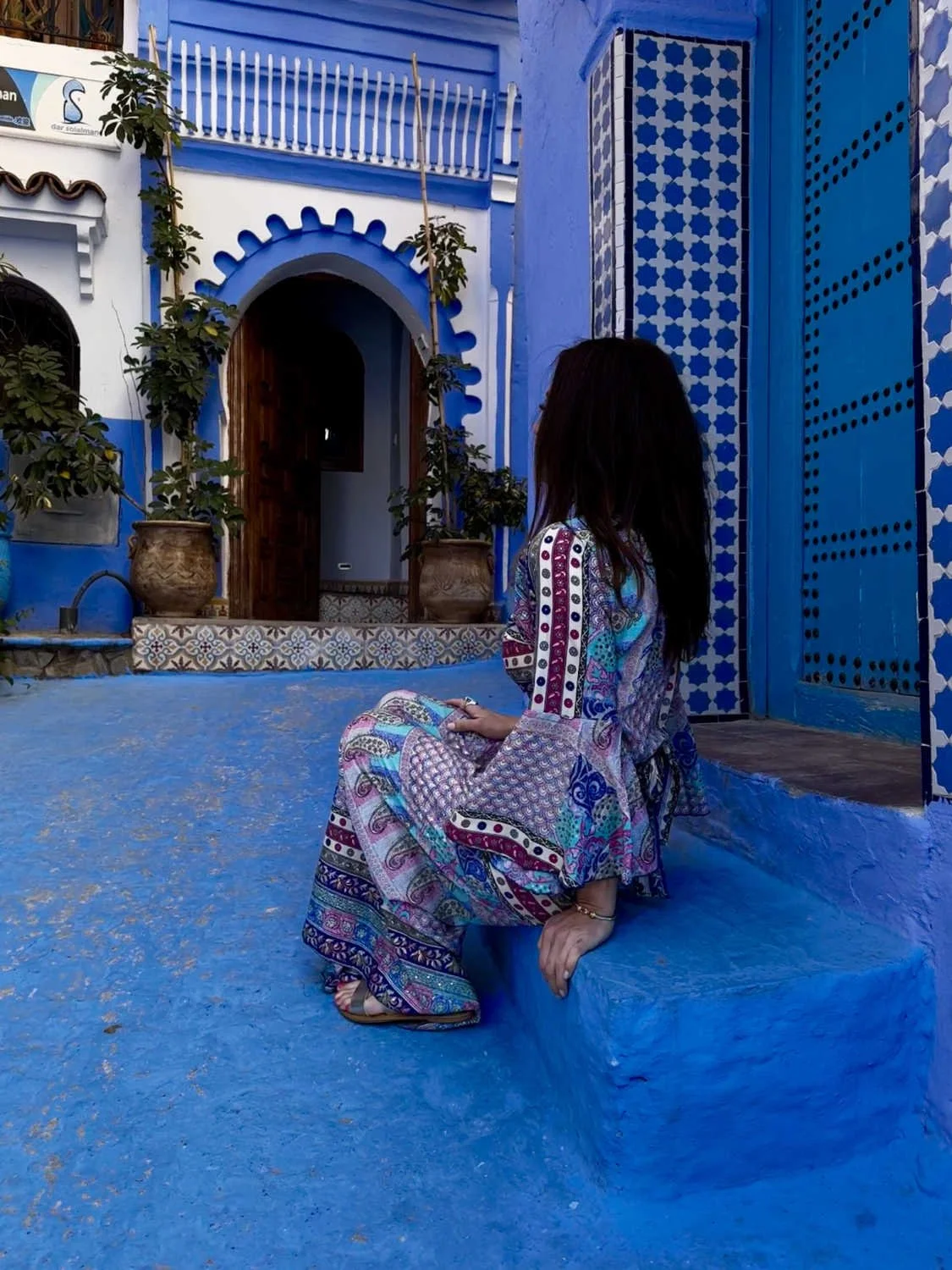 A woman sits on a blue step in a vibrant blue and white courtyard
