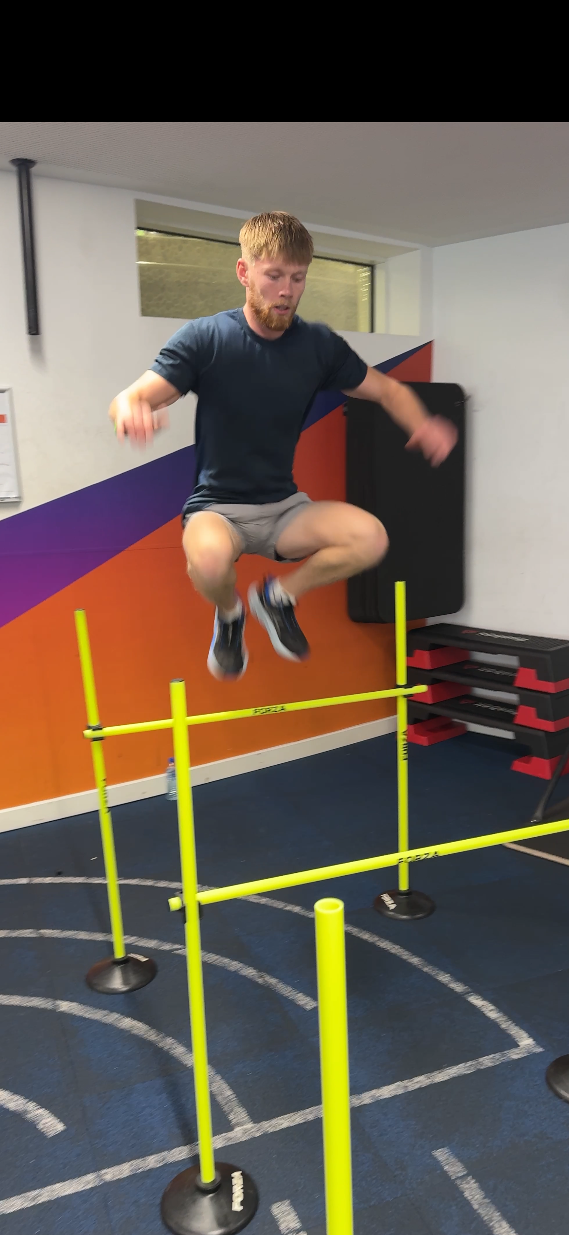 Man jumping over agility hurdles in a gym.