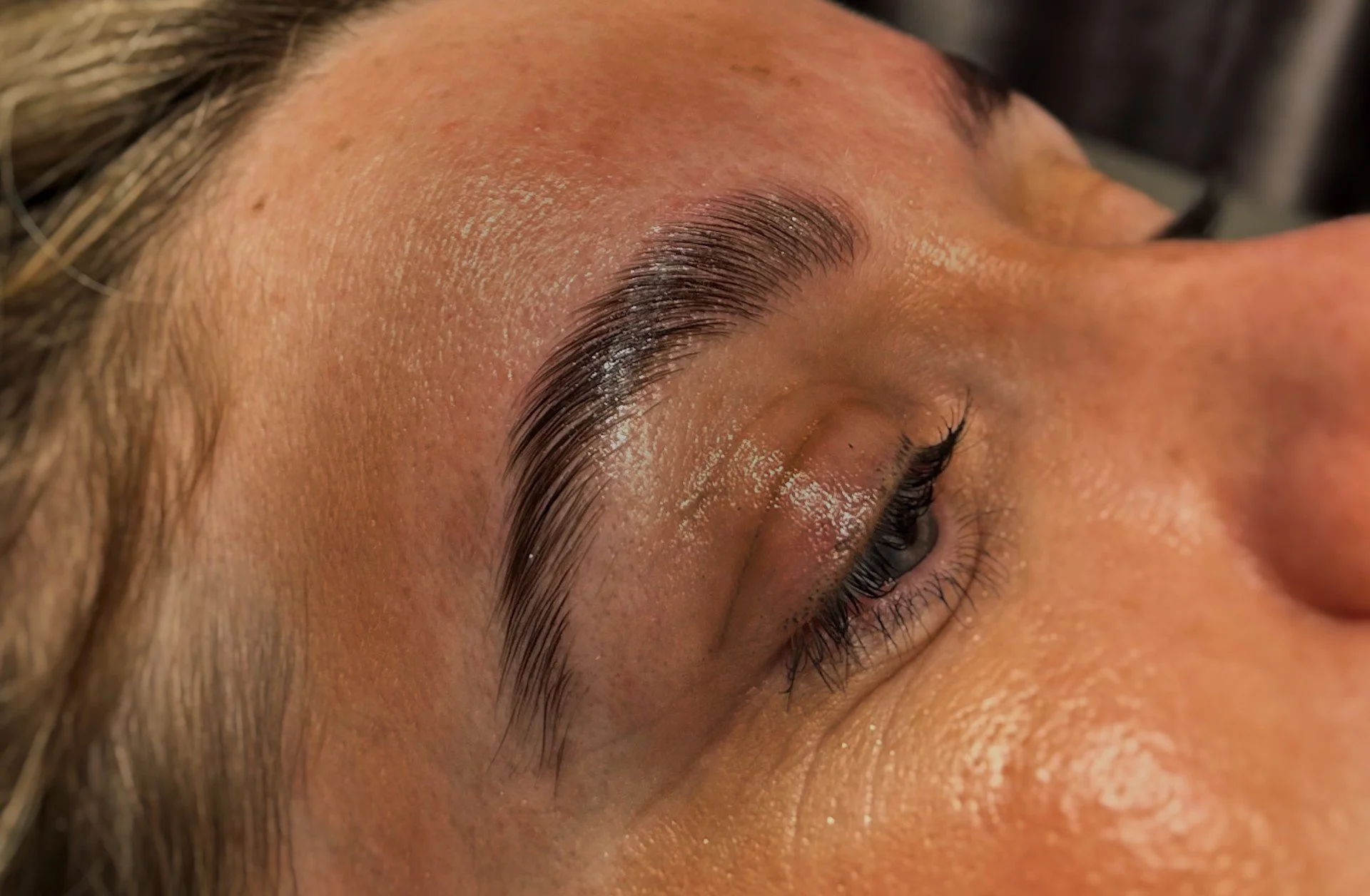 Close-up of a person's eye with well-groomed eyebrows and long eyelashes, with natural skin texture visible.