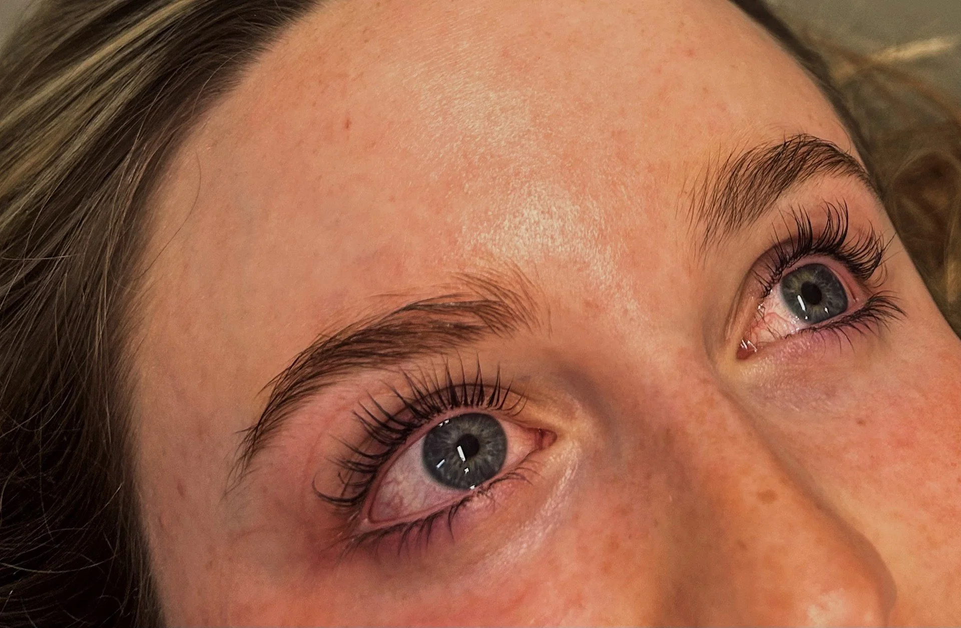 Close-up of a woman's face, focusing on her eyes and forehead, showing natural skin, eyebrows, and long eyelashes.