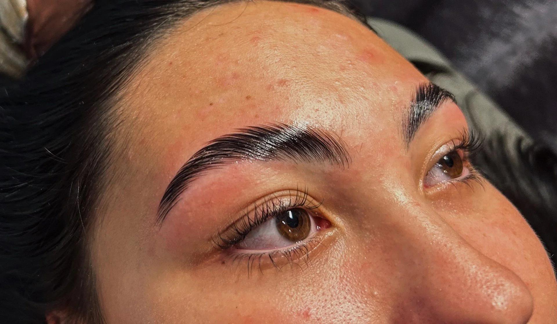 Close-up of a woman's face focusing on freshly shaped and groomed eyebrows, with clear skin and brown eyes.