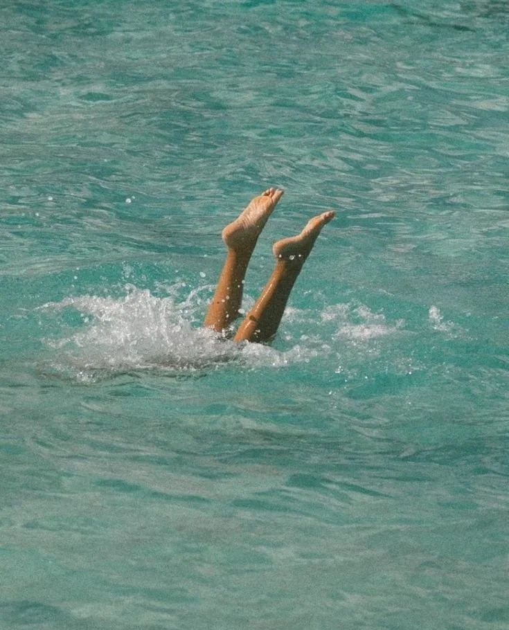 Person submerged underwater with only legs and feet visible, as they appear to be flipping or diving in a swimming pool.