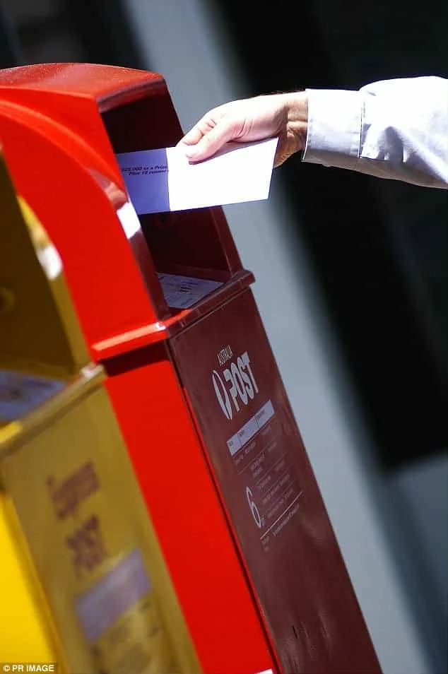 A man's hand returning postal vote for City of Albany Council Election into Australia Post Box