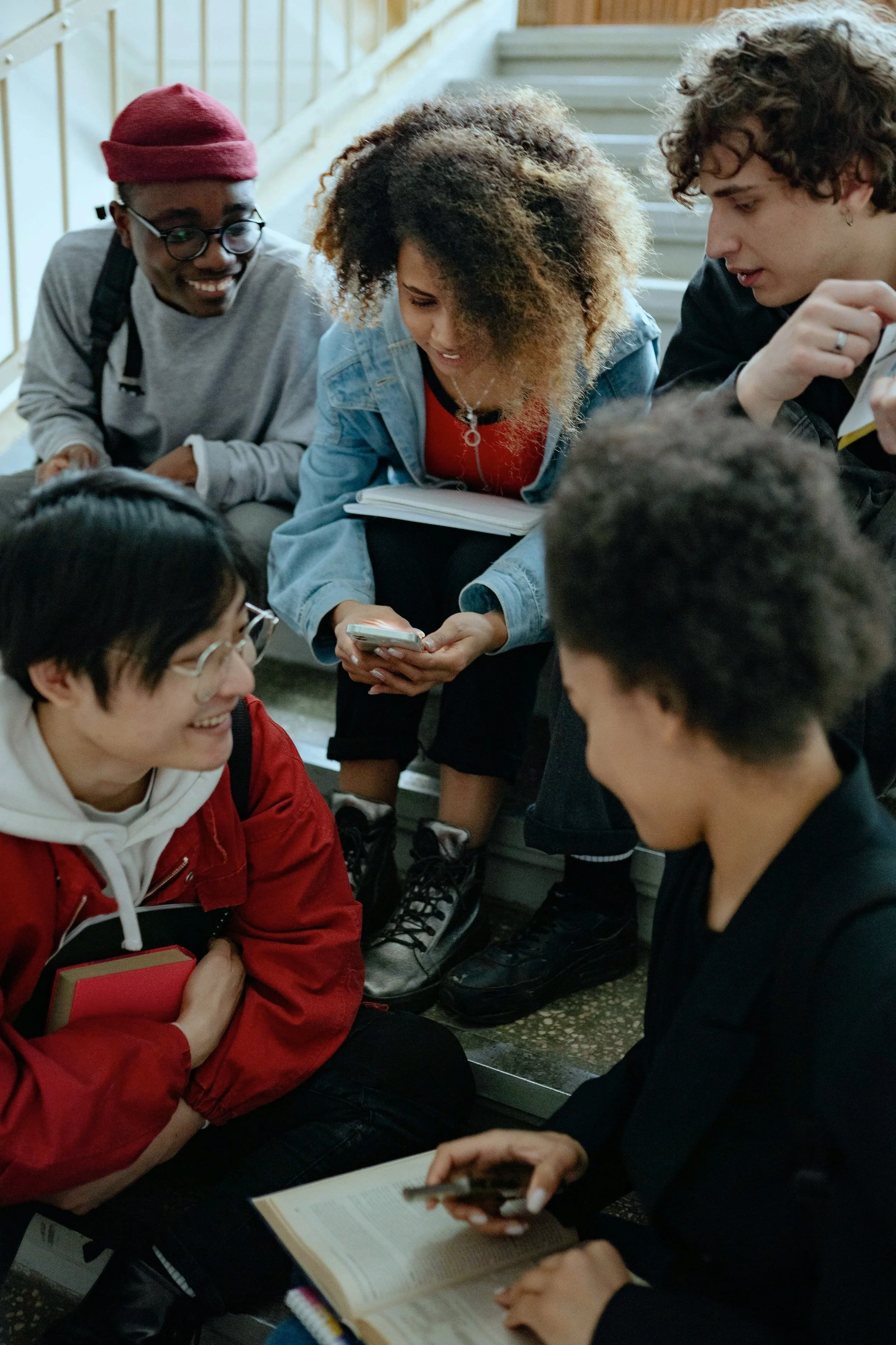 Group of diverse young people sitting on stairs, looking at their phones and talking.