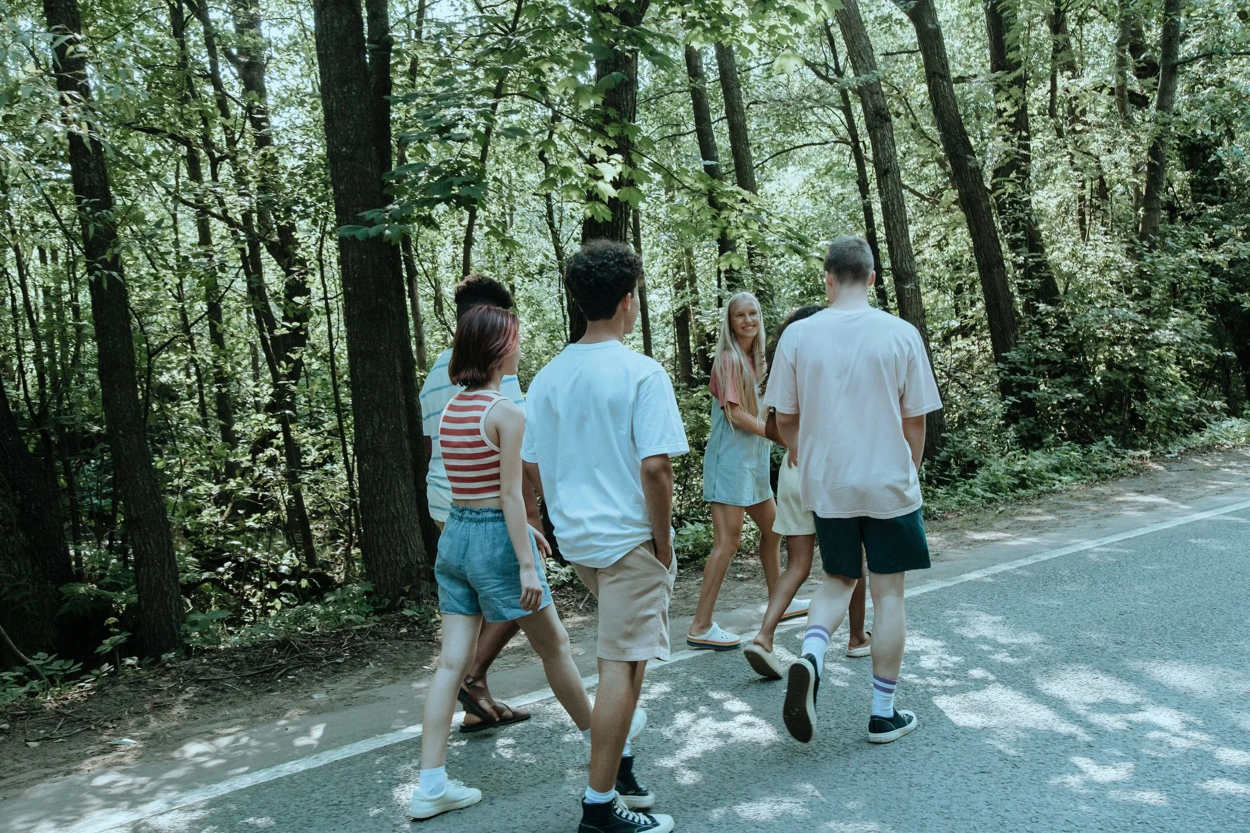 A group of young people walking and chatting along a wooded trail in a forest.