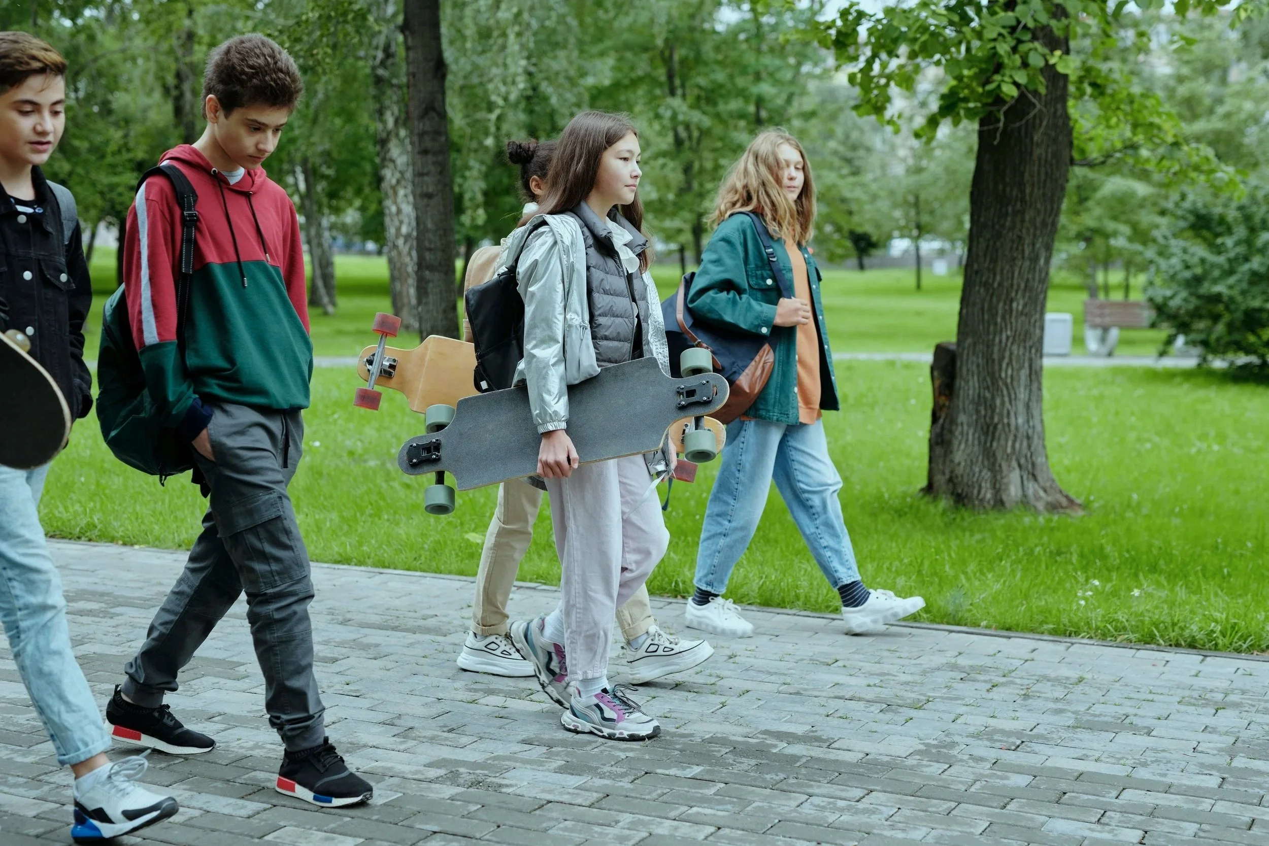 A group of teenagers walking in a park, one girl carrying a skateboard.