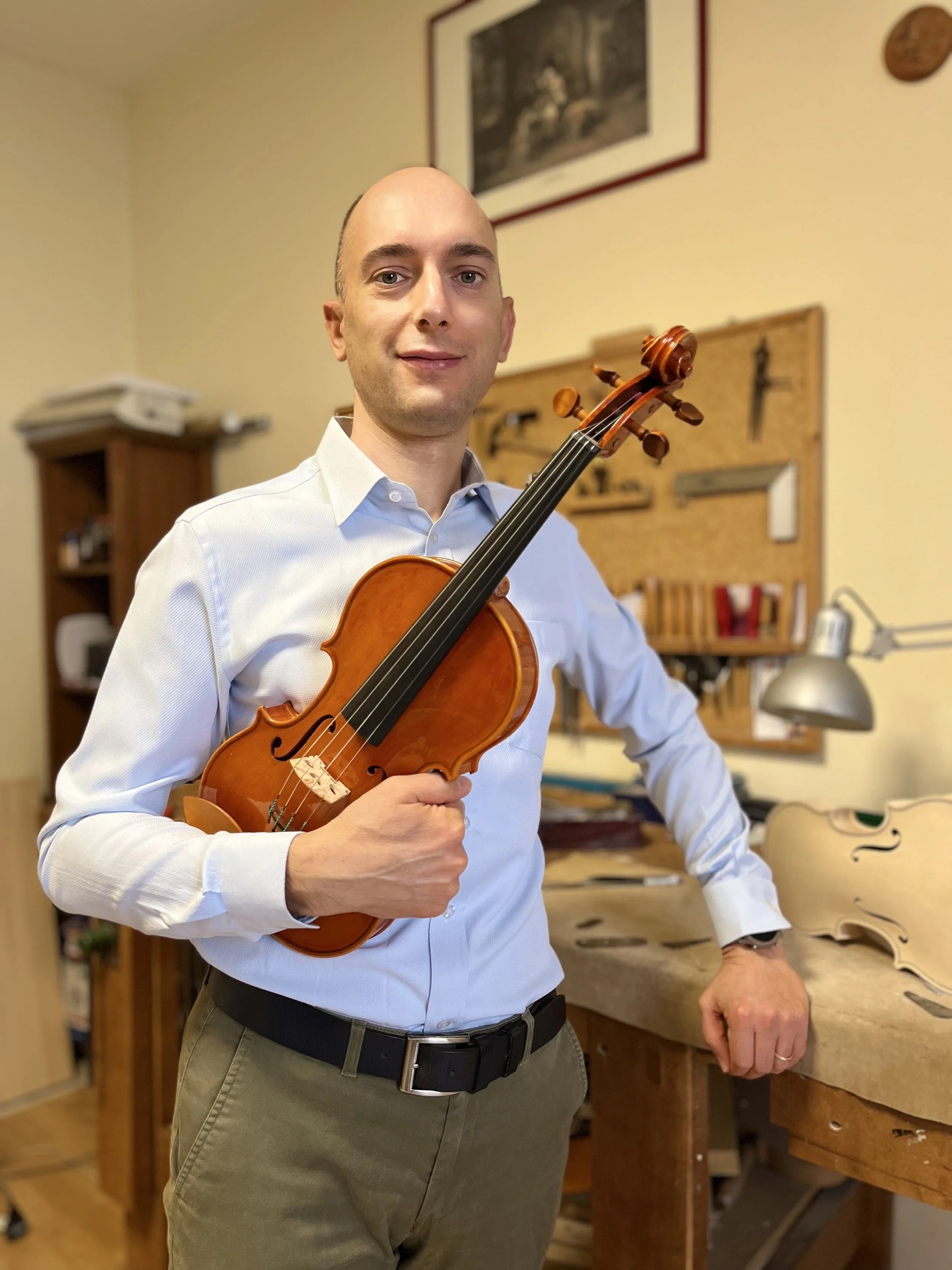 Marco Osio holding a handmade violin in his Cremona workshop