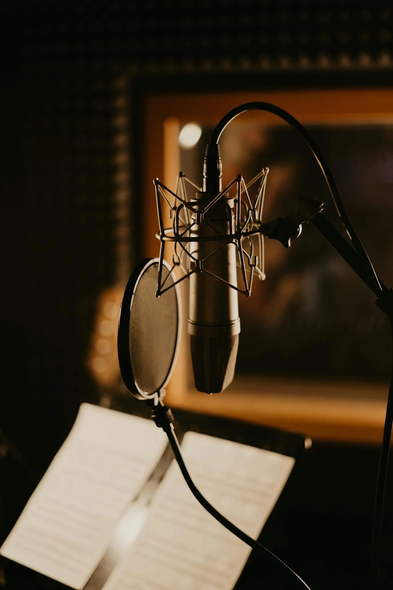 A professional microphone on a stand with a pop filter in a recording studio, with sheet music and a music stand in the background.