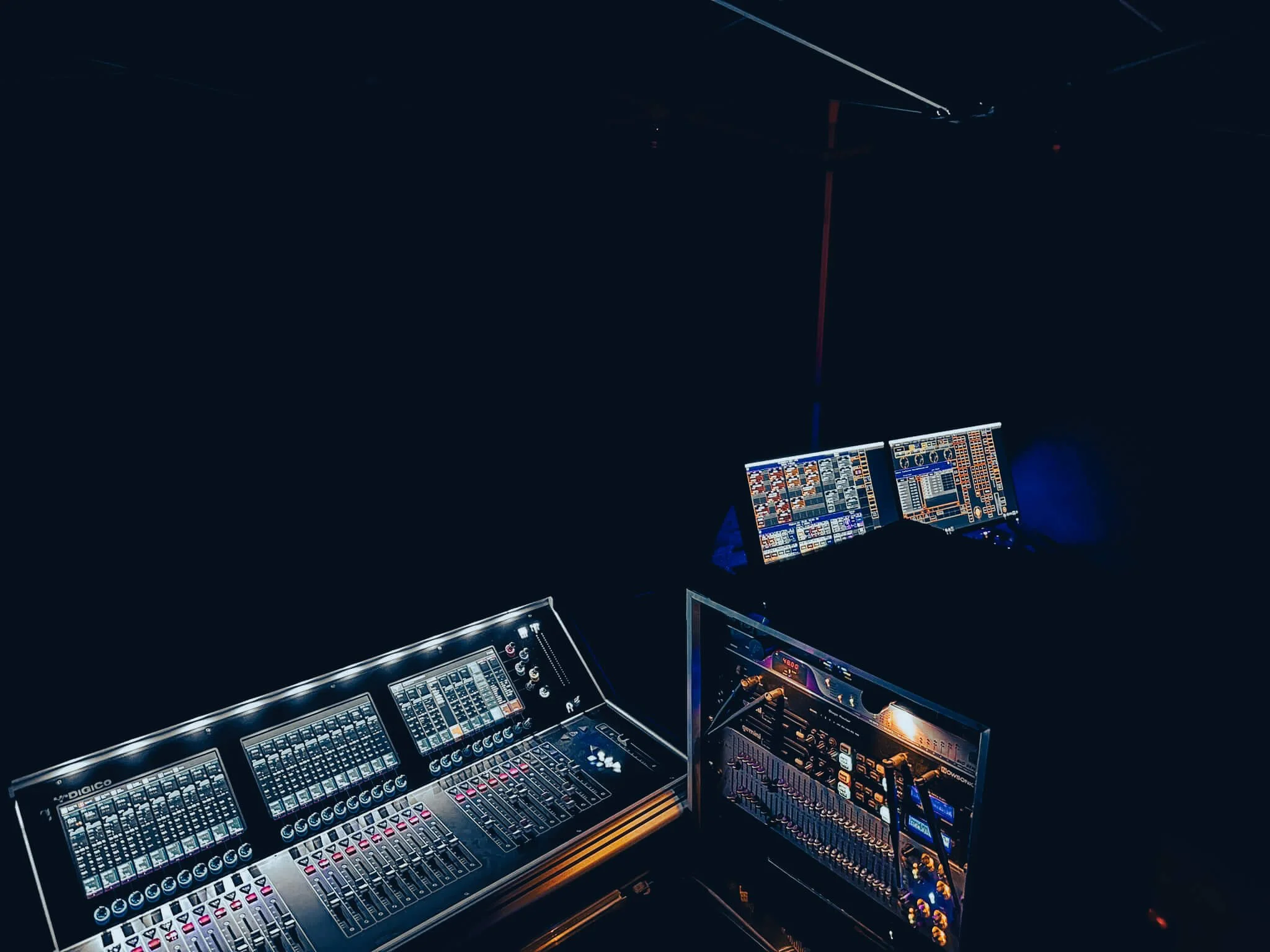 Lighting and sound equipment at a stage, including a sound mixer, two monitors, and a digital audio control console in darkness.