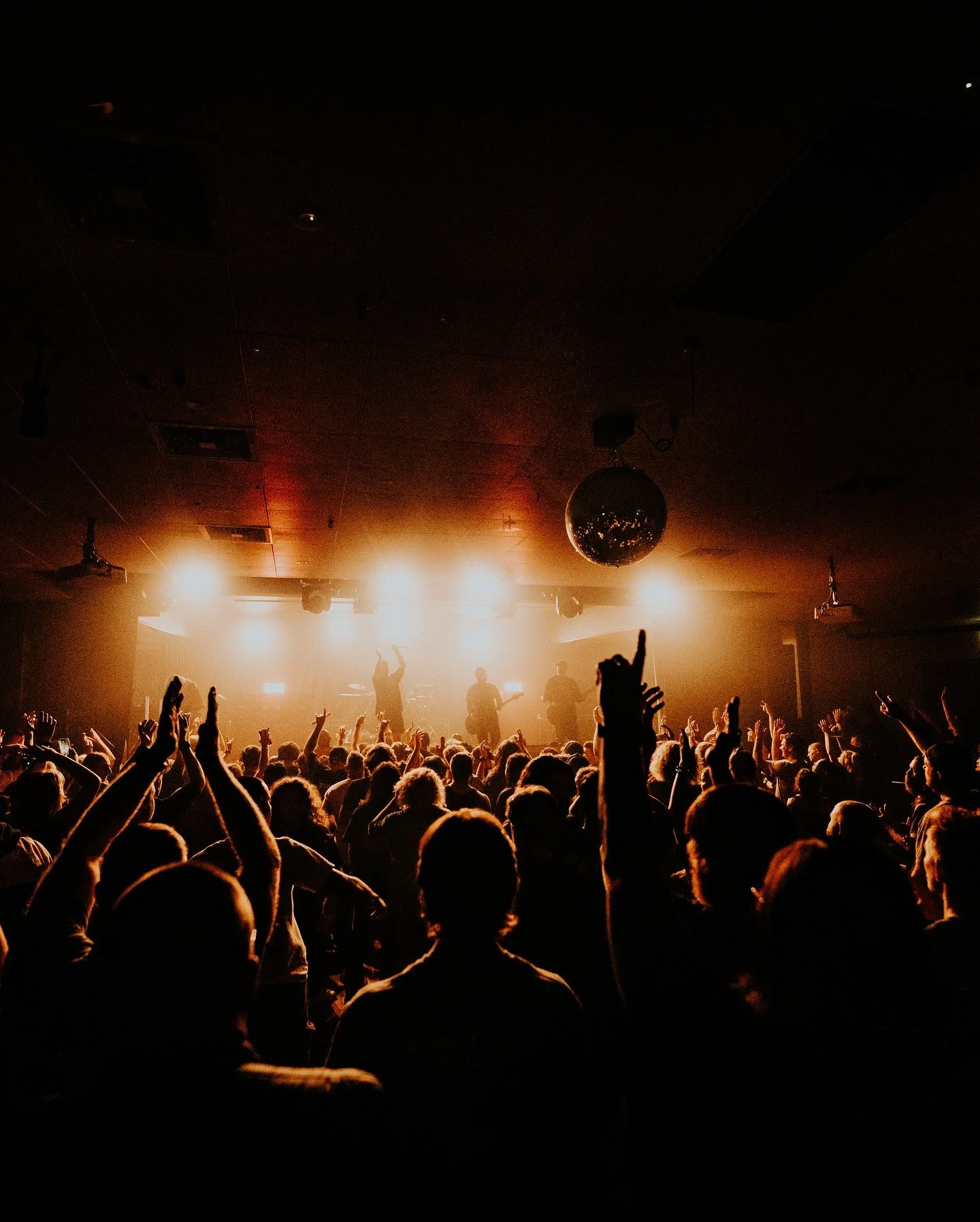 Concert crowd at a show, facing a stage bathed in bright orange light