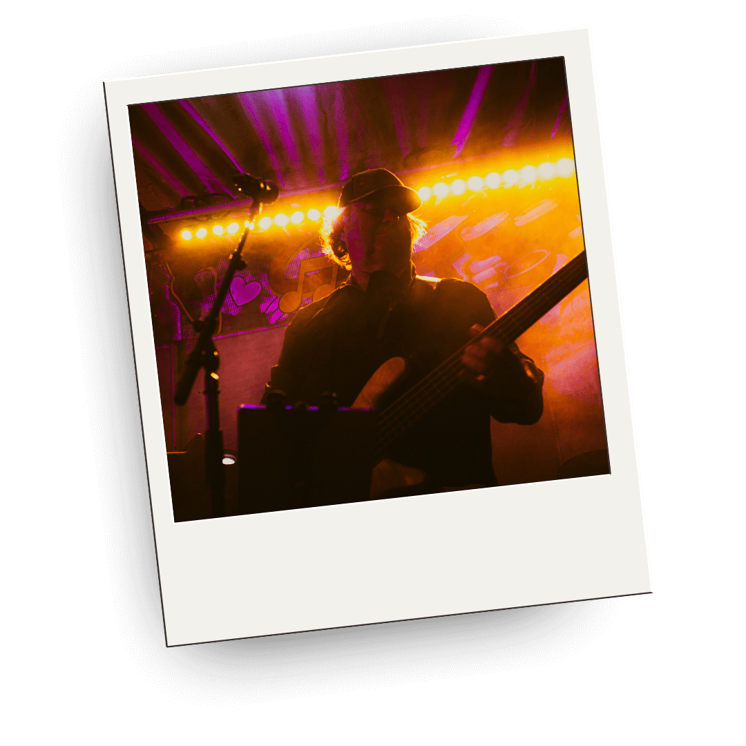 Polaroid picture of Fat Man from Savage Groove playing a guitar on stage with colorful lights.