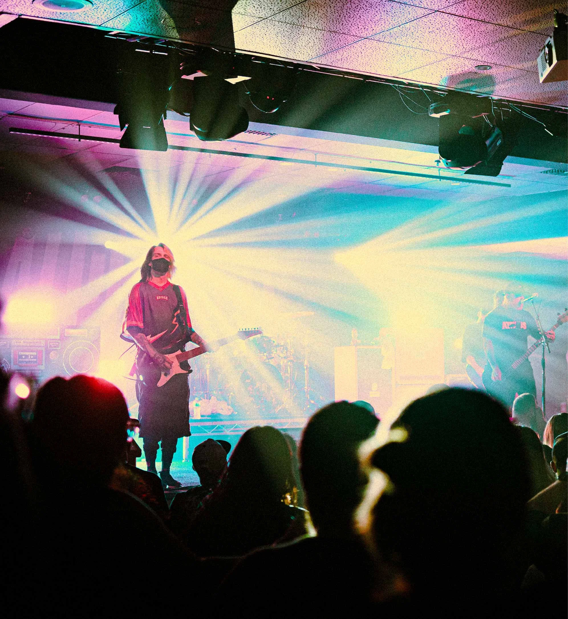 The band Alpha Wolf performing on stage with colorful, radiant lighting and an audience watching.