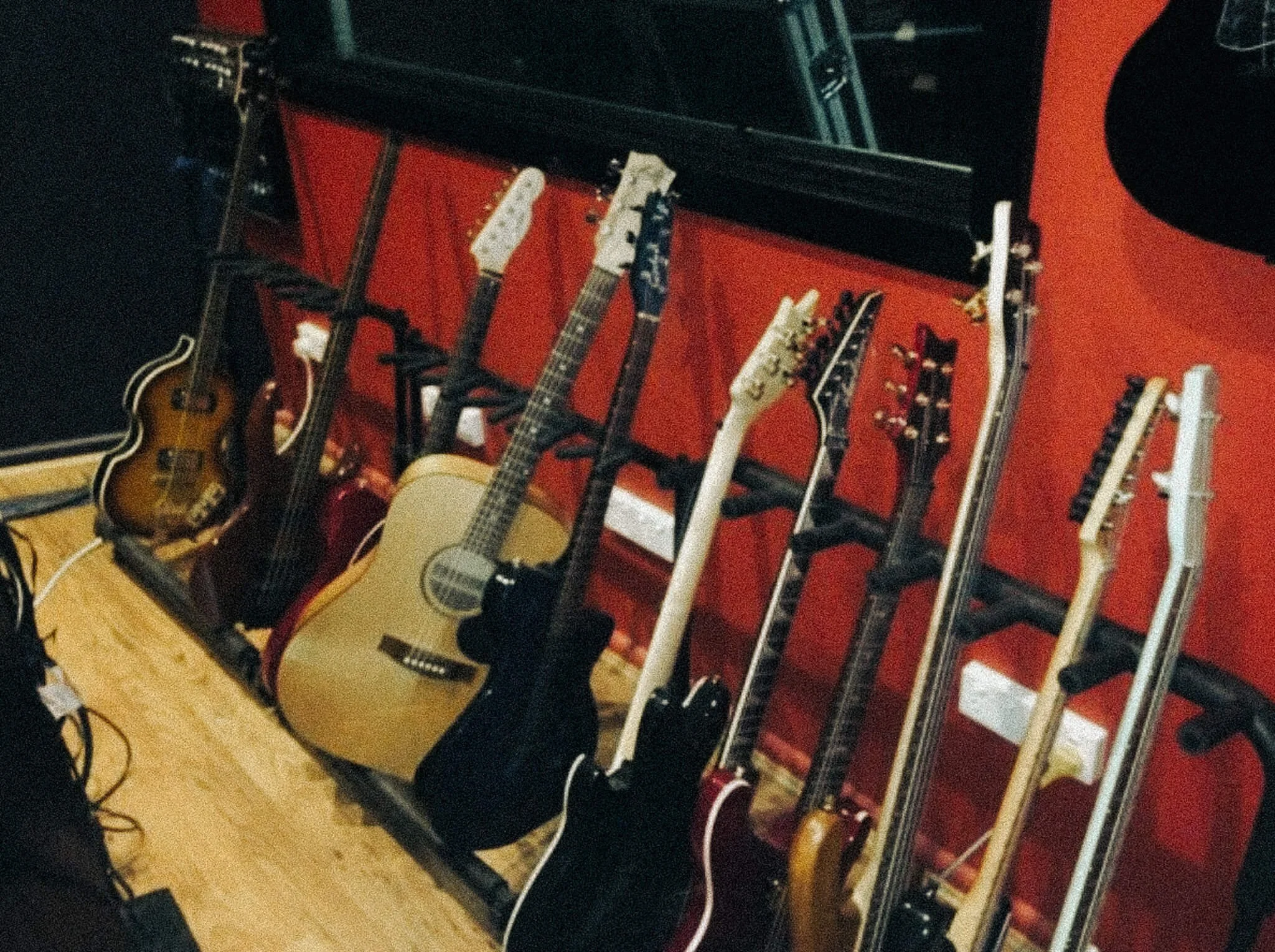 A row of electric and acoustic guitars hanging on a black rack against a red wall in a music studio.