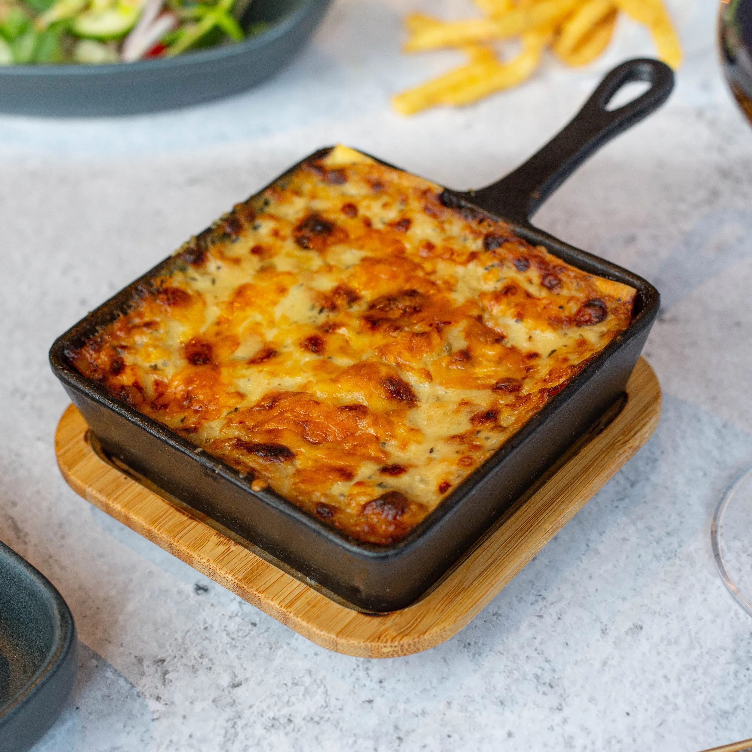 Baked cheesy casserole in a black cast iron dish on a wooden board.