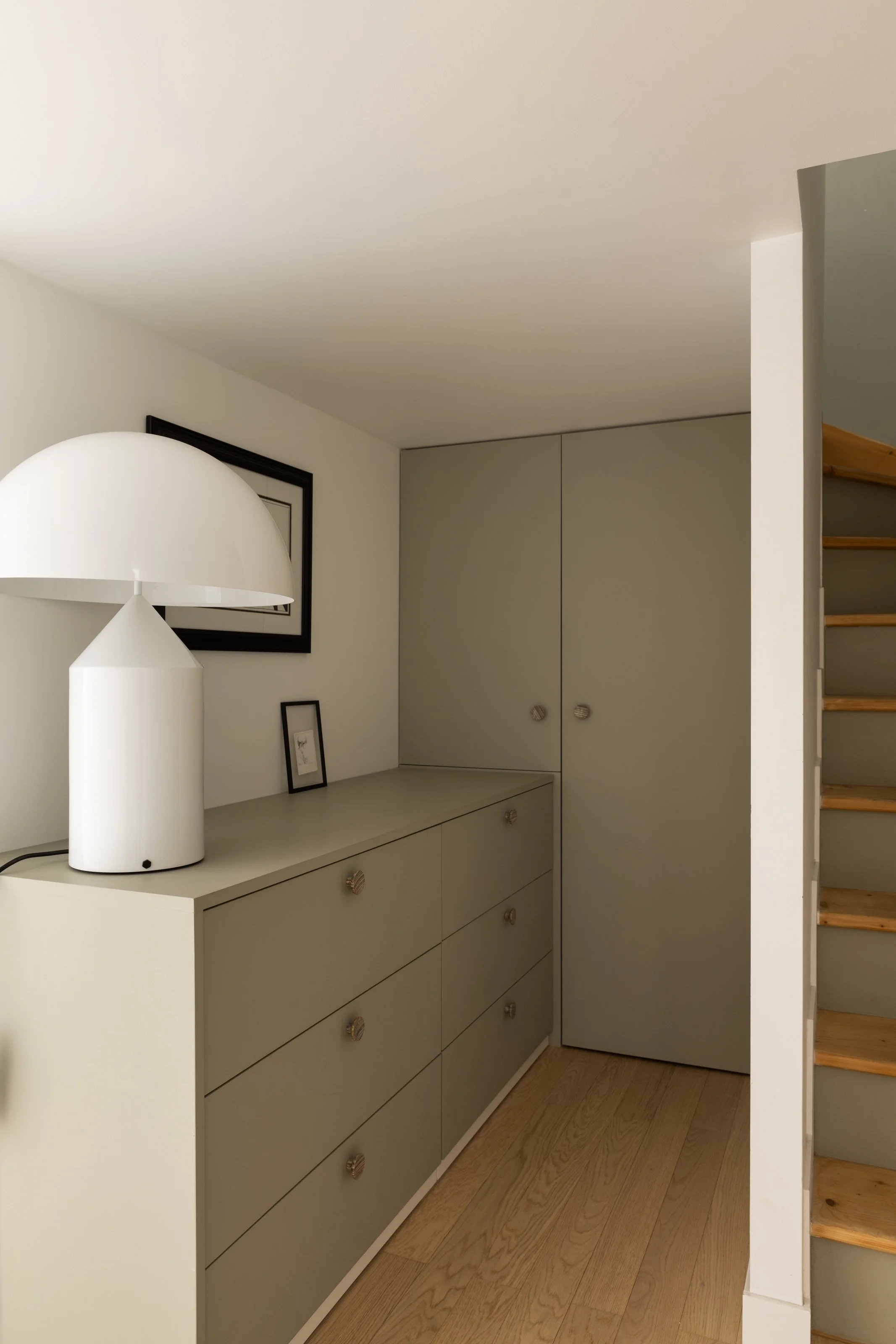 Un meuble gris avec des tiroirs et un placard dans un intérieur moderne, avec une lampe blanche sur le dessus et des cadres photo accrochés au mur.