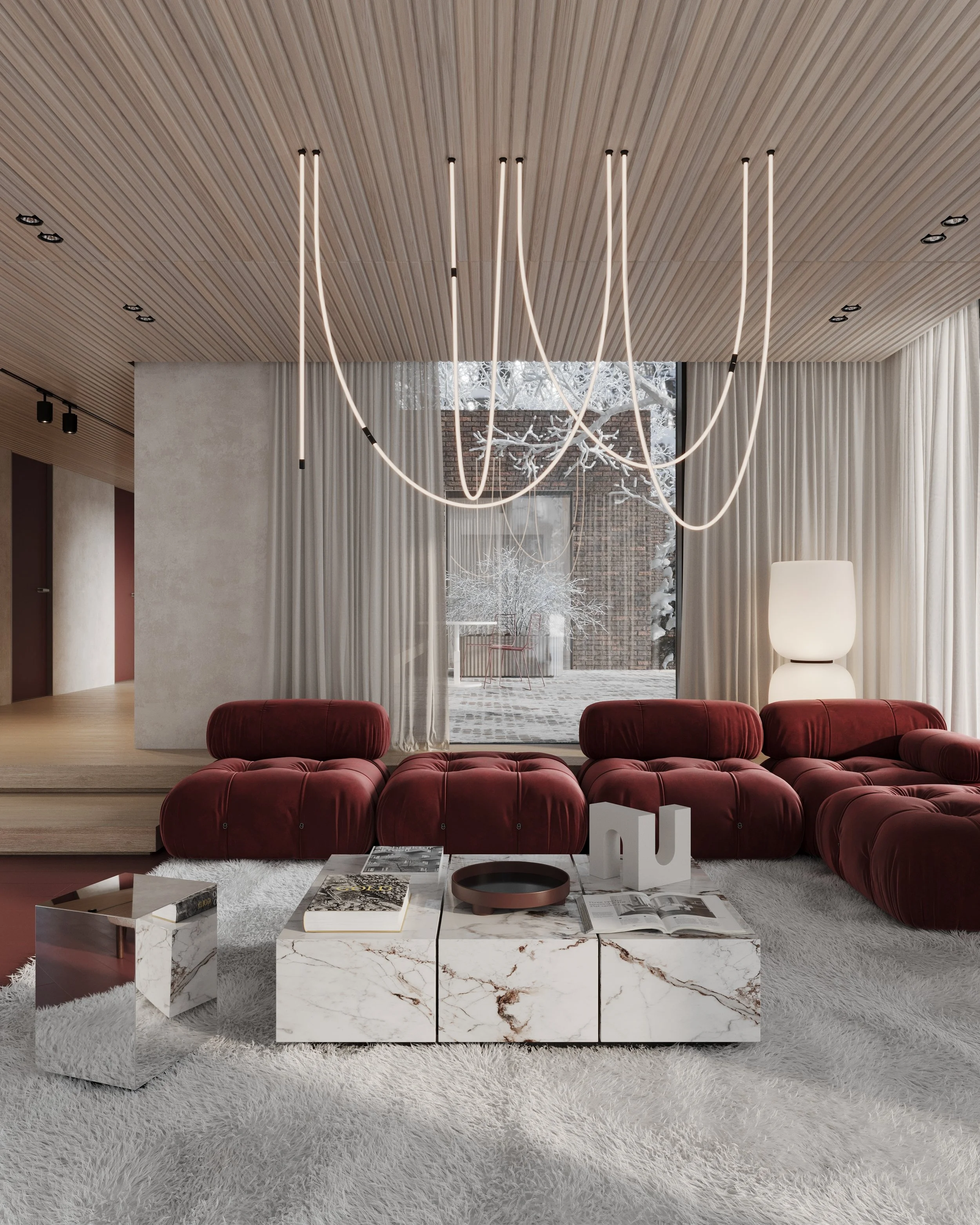Modern living room with red velvet couches, marble coffee tables, and minimalist lighting fixtures, overlooking a snowy outdoor scene through large windows with sheer curtains.