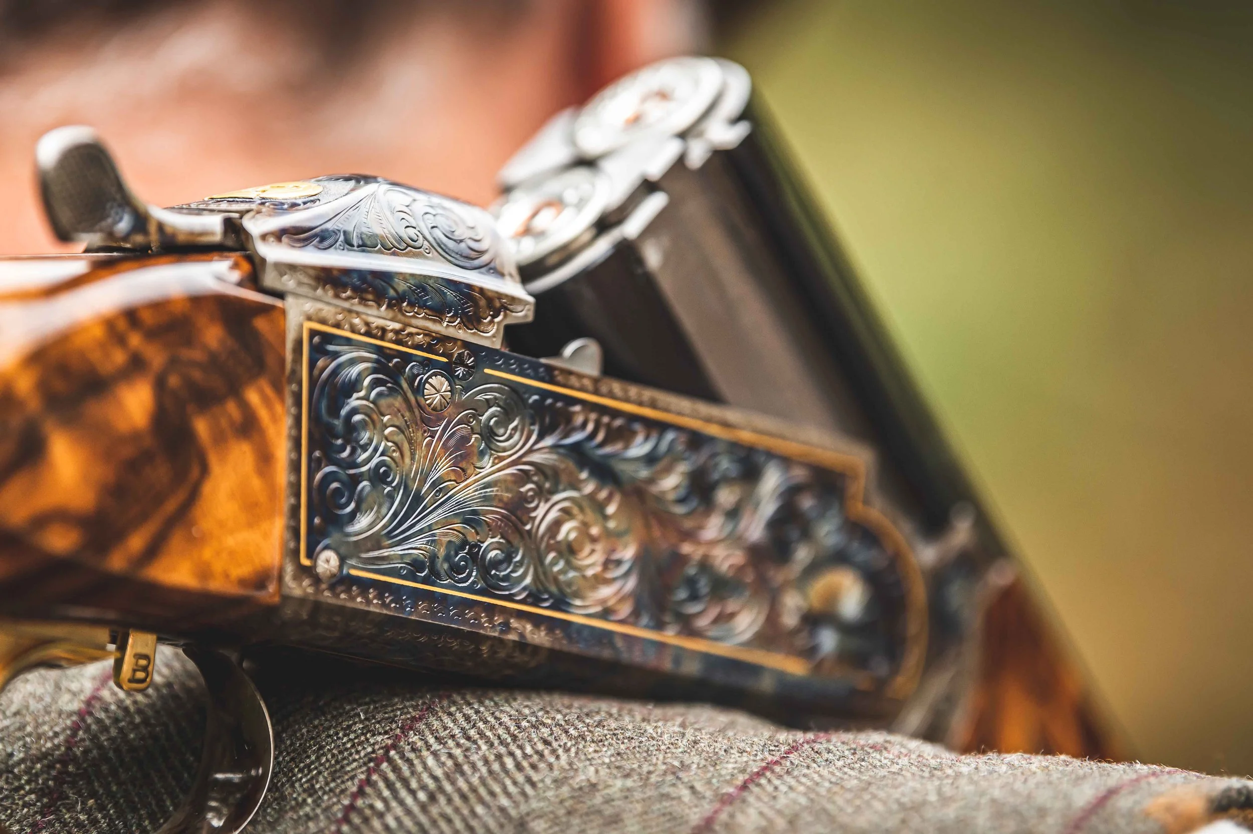 A close-up of an engraved shotgun resting on a tweed-clad shoulder.