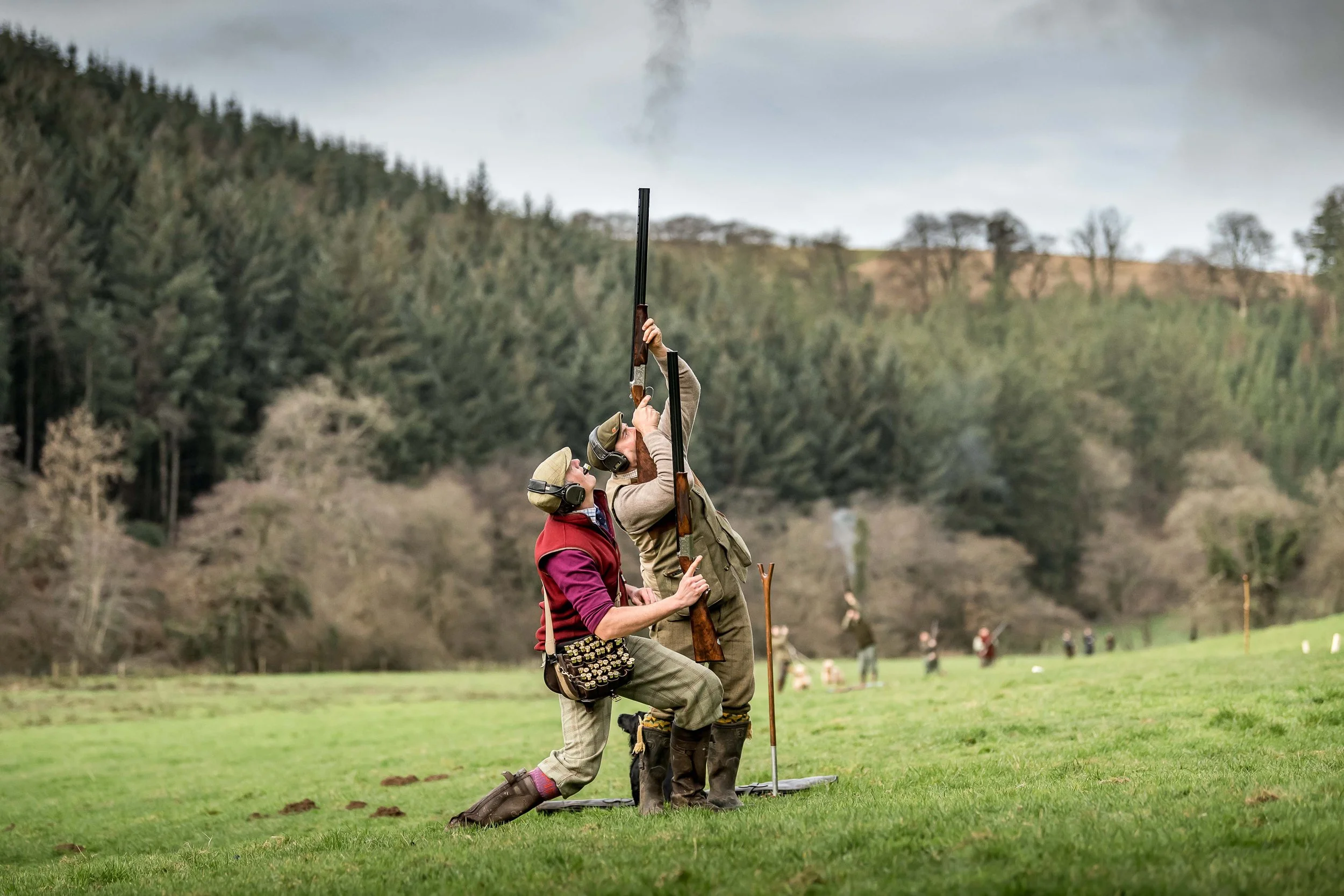 A shooting party on the Loyton estate with two men in traditional attire firing shotguns.