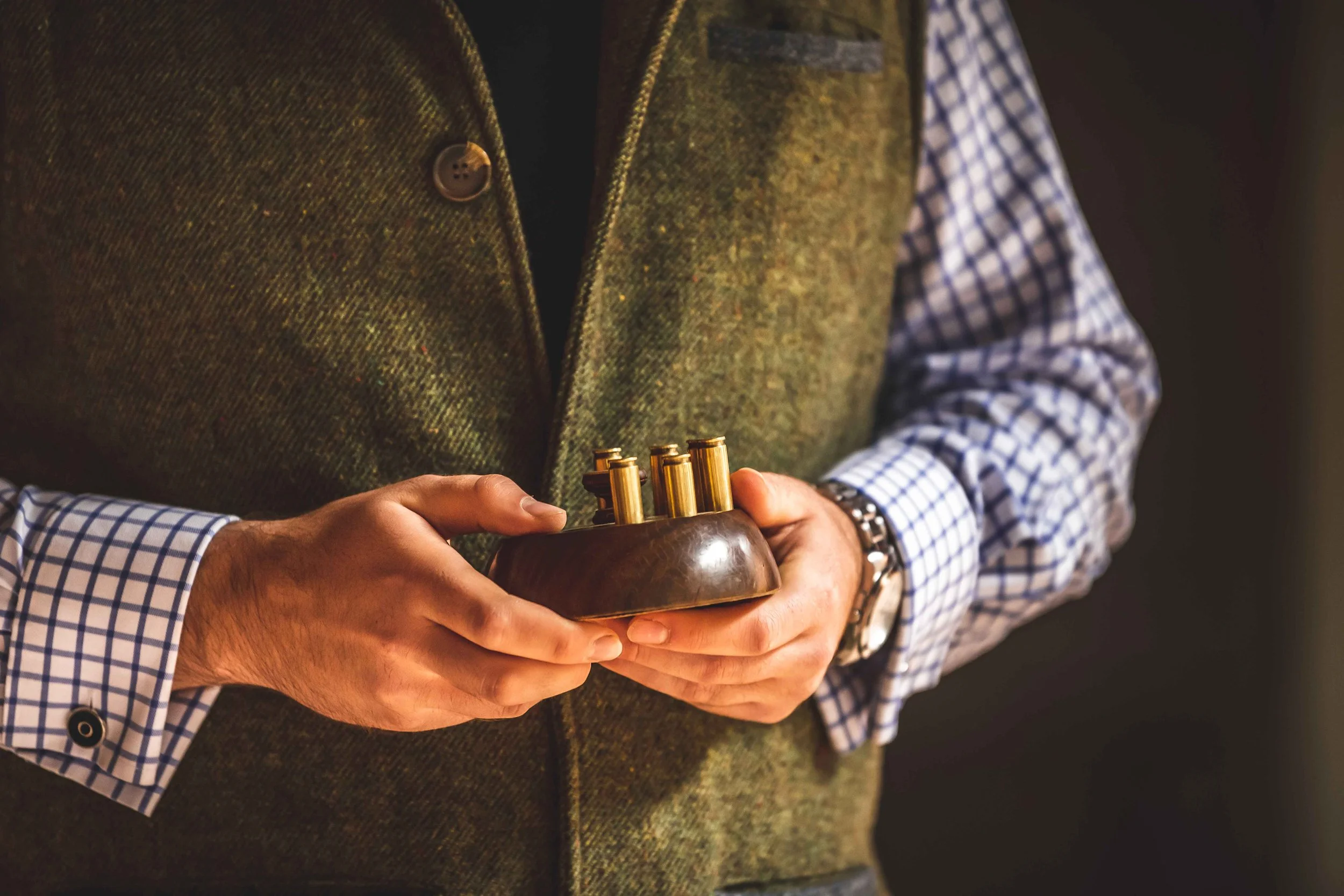 A person in a tweed waistcoat holding brass position pegs used for drawing lots at a Loyton shoot.