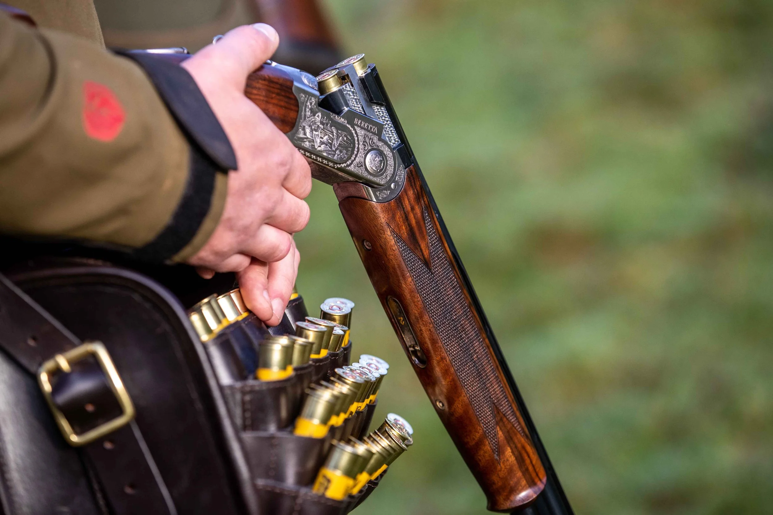 Close-up of a person loading a Beretta shotgun from a leather cartridge bag during a Loyton shoot.