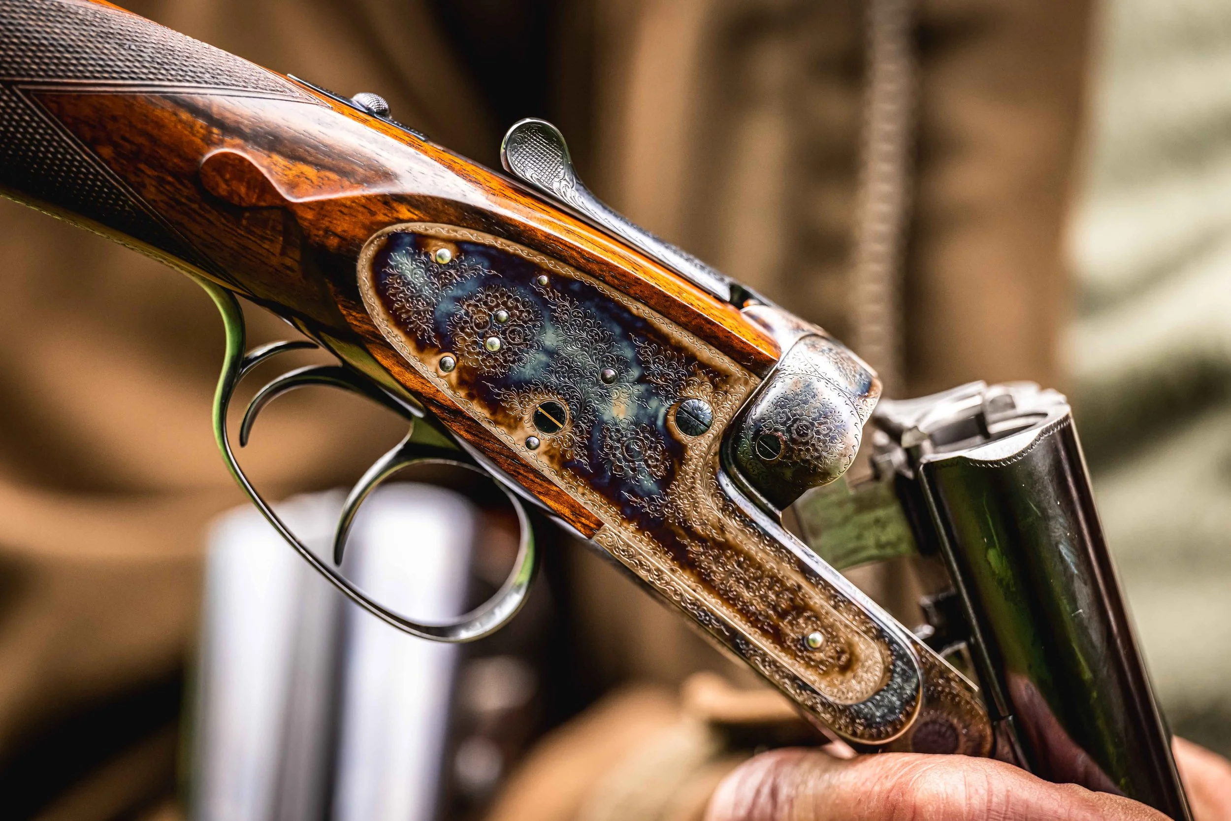 Close-up of a side-by-side shotgun with fine scroll engraving, held in an open position.