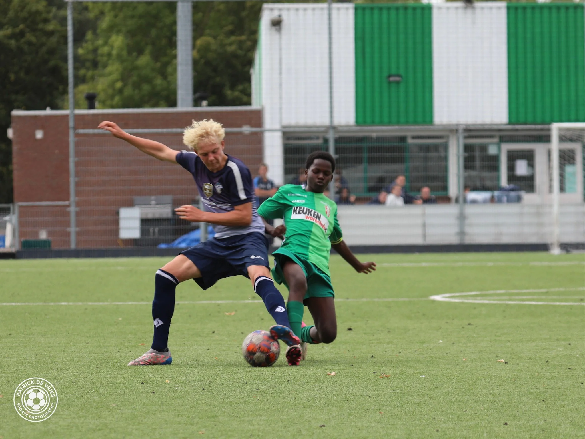 Twee jonge jongens spelen ijshockey op een grasmat, een in een blauw uniform en de ander in een groen uniform, beide proberen de bal te veroveren.