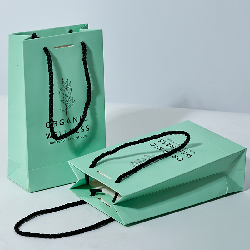 Green luxury paper bag with black artwork and ribbon closure, perfect for premium gifting.