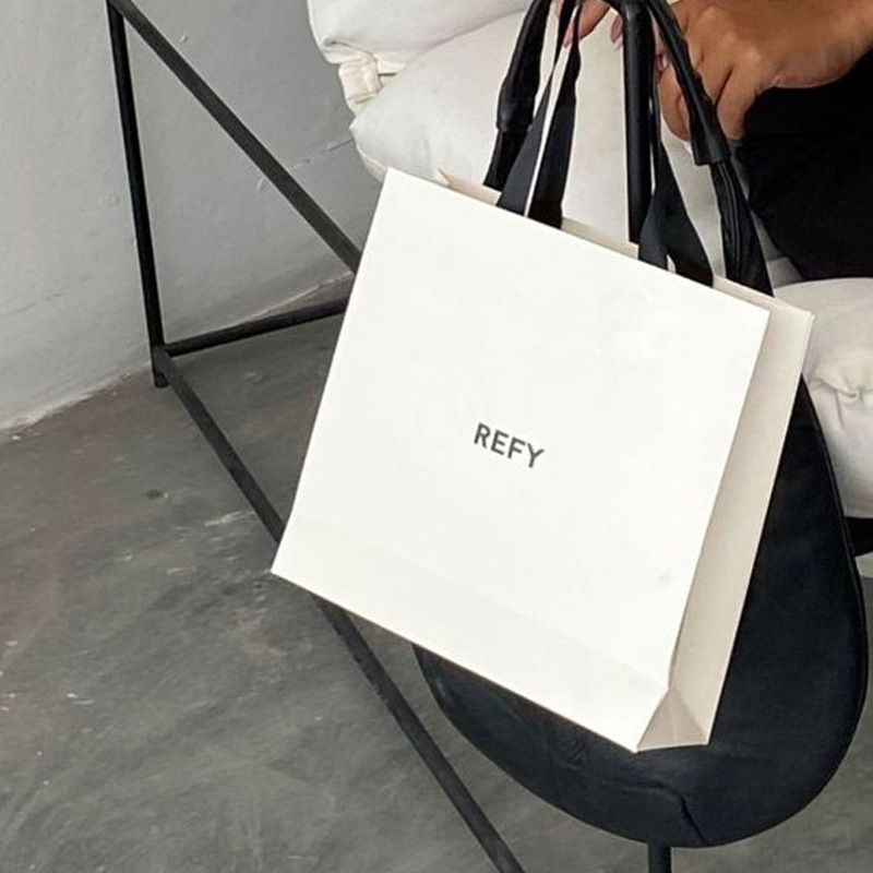 White matt laminated gift bag with black logo and integrated black ribbon handles, ideal for retail gift bags.