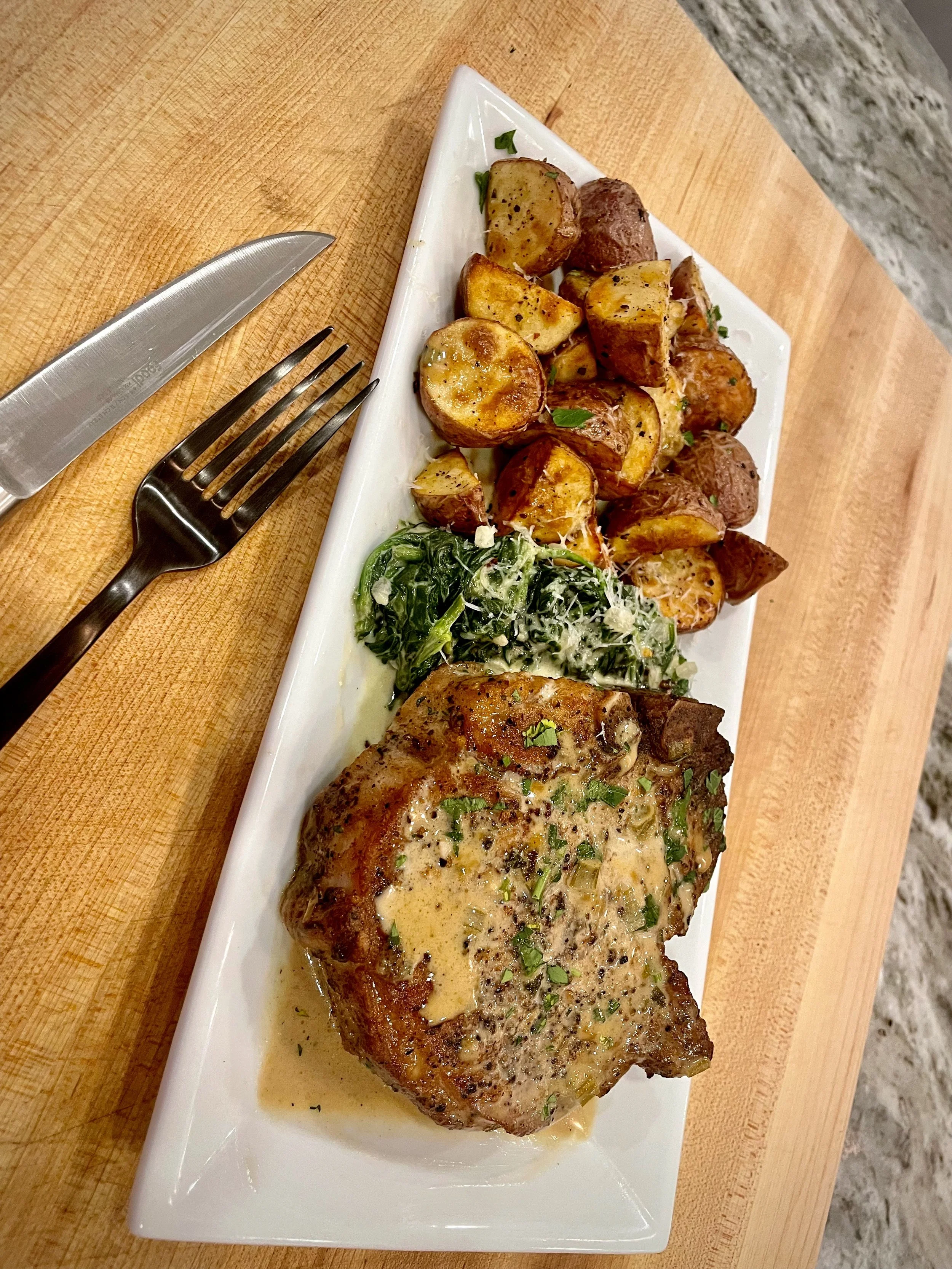 Plate of roasted chicken thigh with potatoes and greens on a white rectangular dish