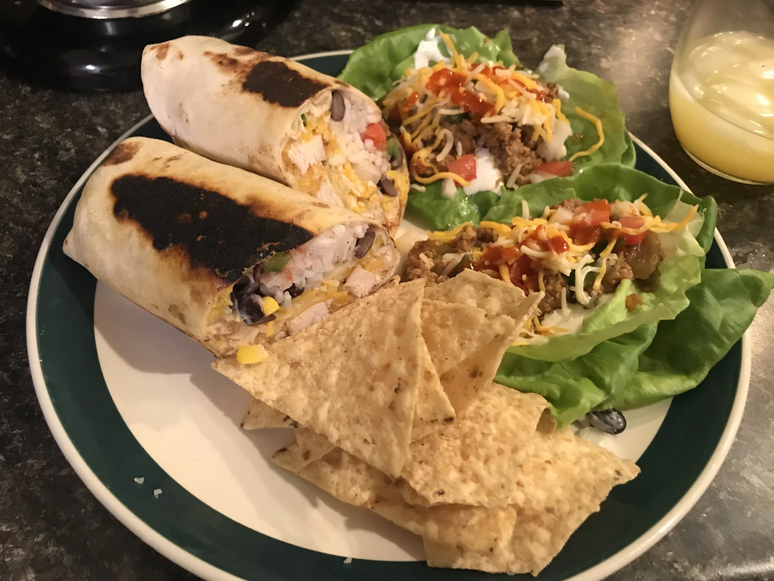 Plate of two grilled burritos, lettuce cups with taco meat, shredded cheese, tomatoes, and sour cream, with tortilla chips and queso on the side.