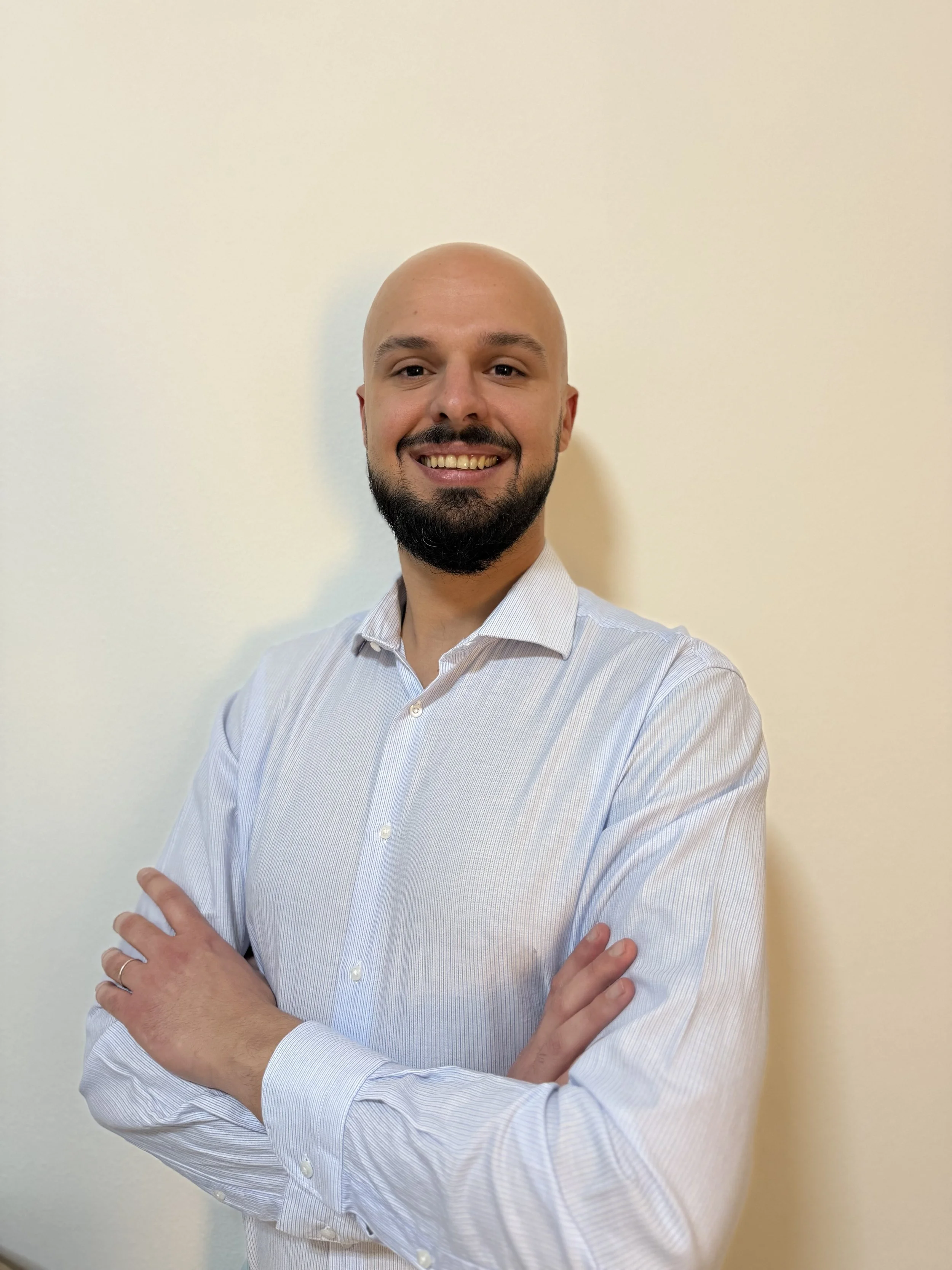 Uomo sorridente con camicia bianca, braccia incrociate, sfondo neutro